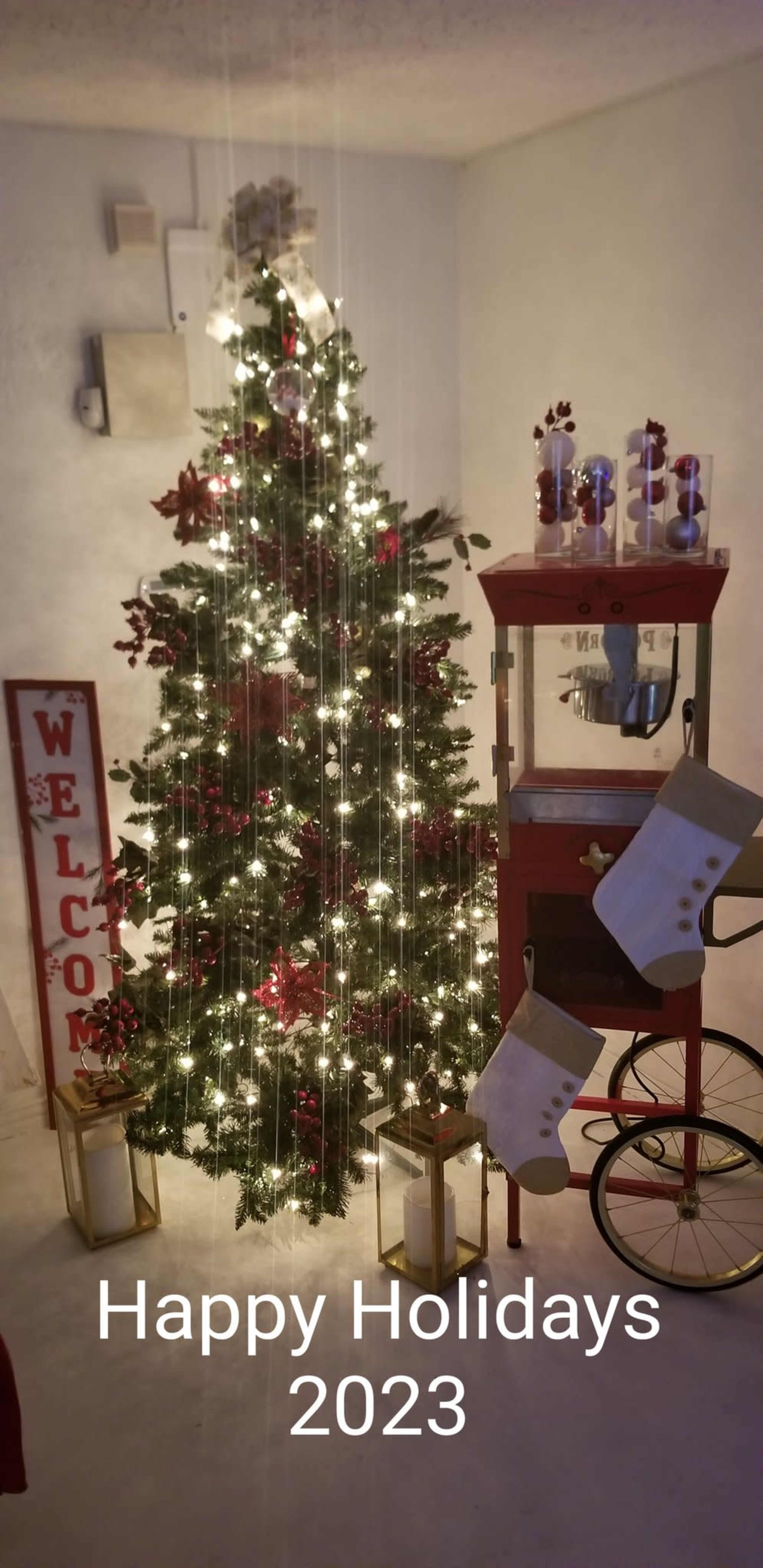 A decorated Christmas tree with lights, a popcorn cart, and stockings, all displayed in a cozy room with a "Welcome" sign.