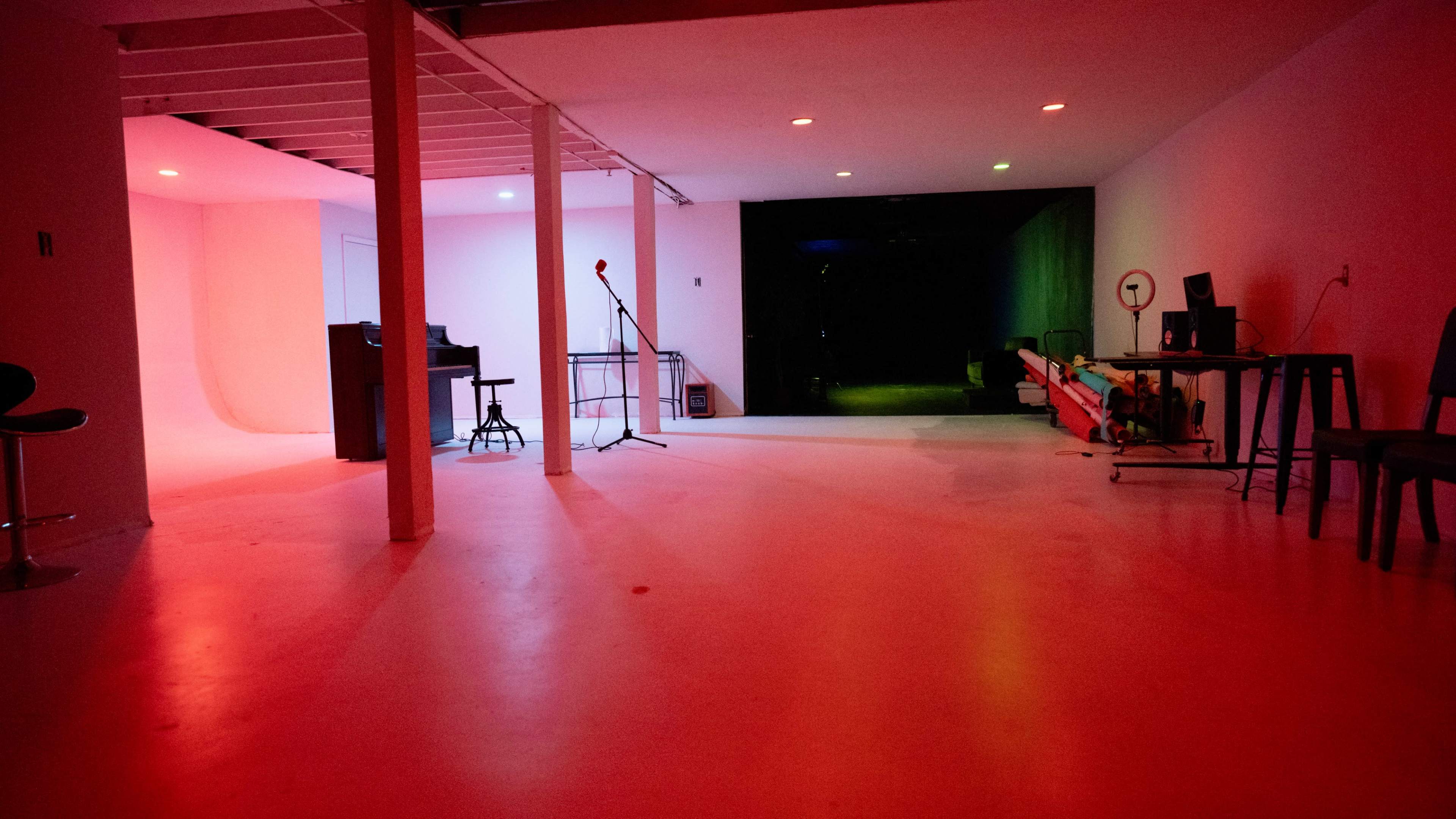 An empty studio space with a mic stand, a bar stool, and various illuminated areas in red and green light.