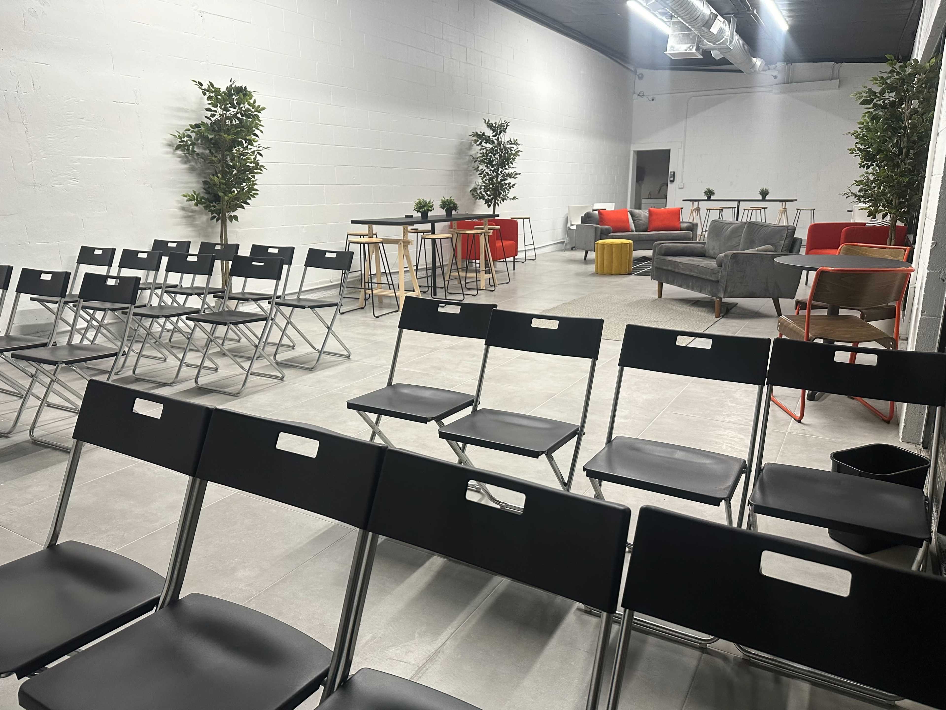 A spacious, modern room arranged with rows of black folding chairs facing a seating area with a couch and tables.