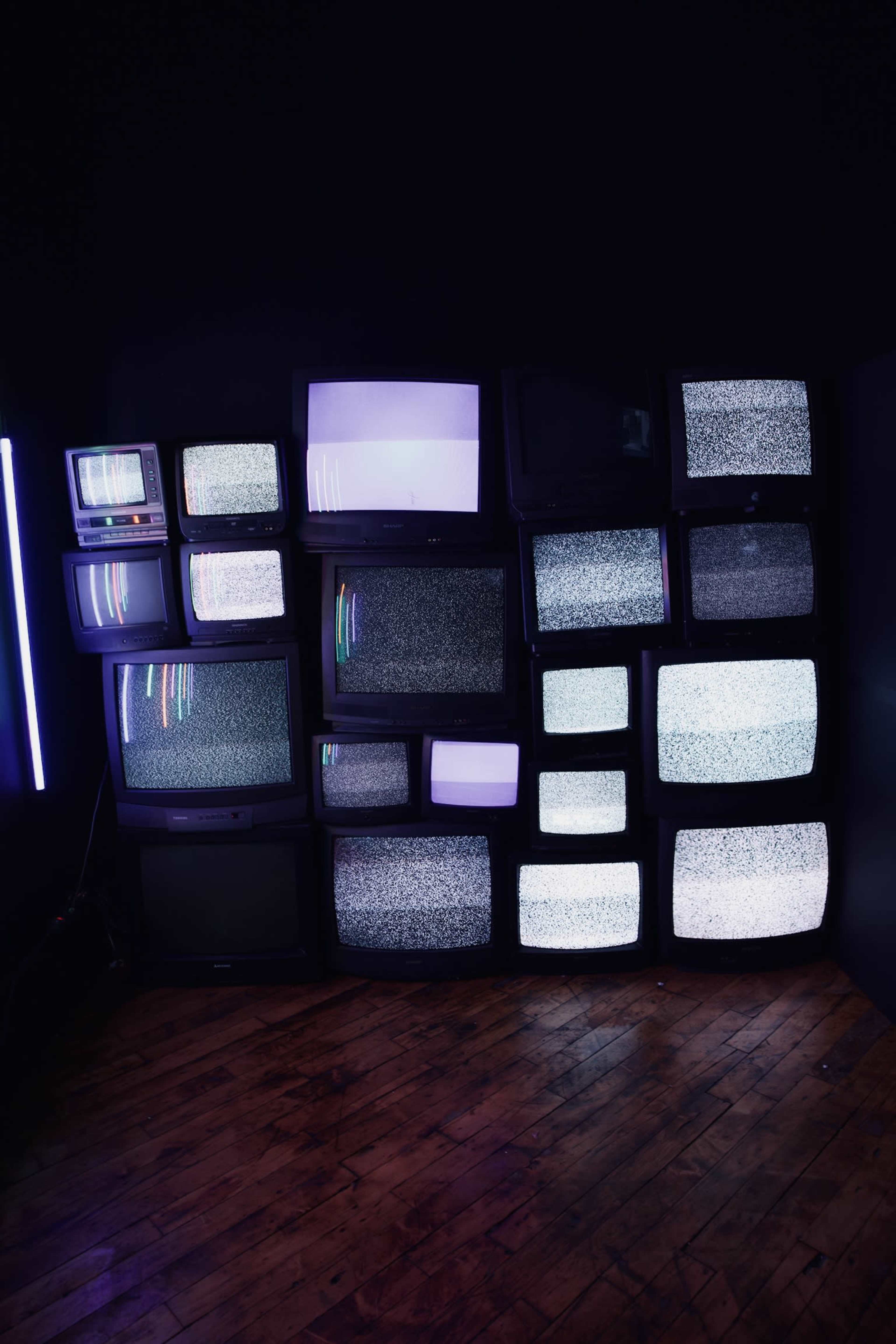 A cluster of vintage televisions displaying static is arranged against a dark wall.