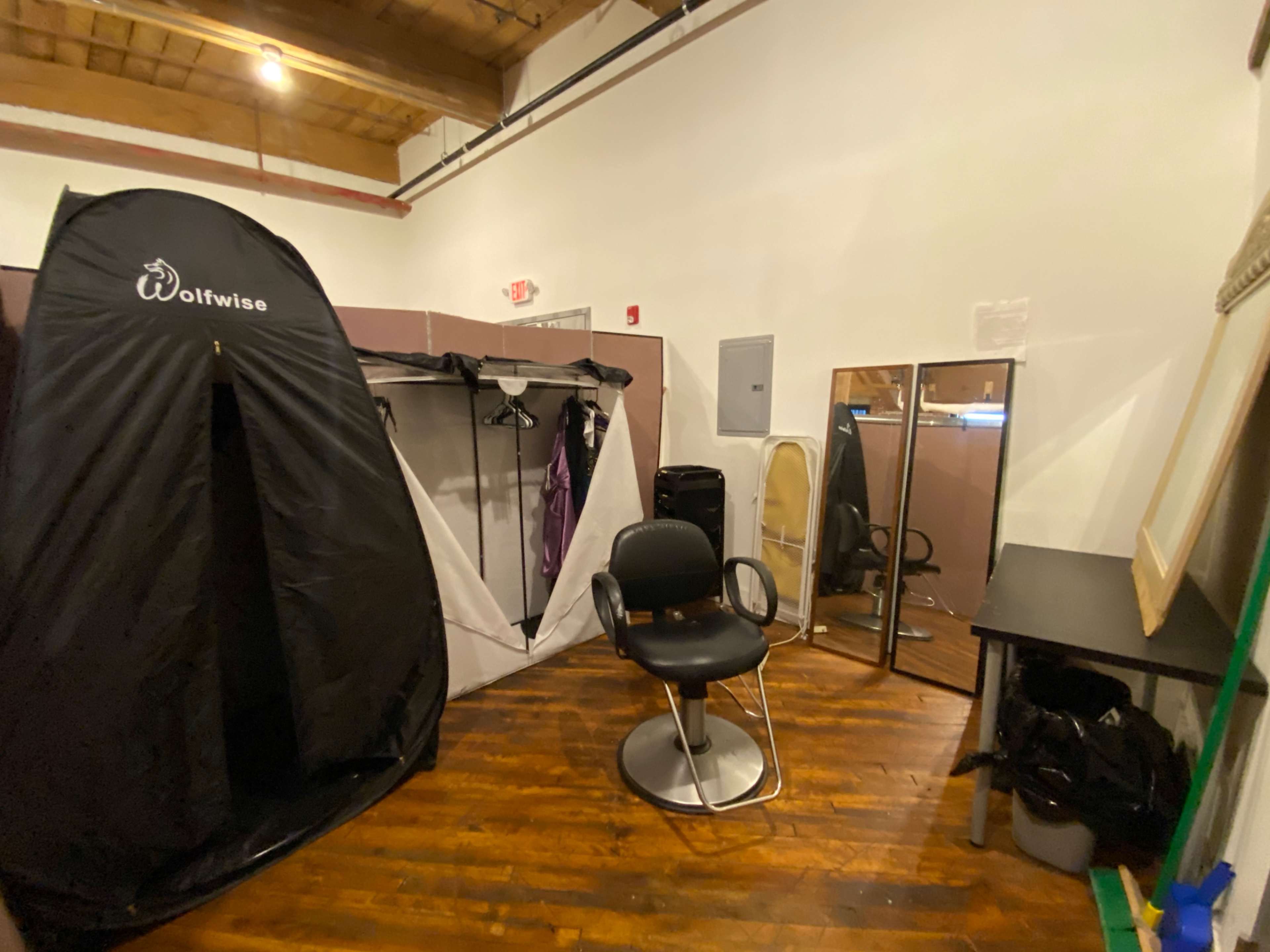 A small room featuring a black privacy tent, a swivel chair, a large mirror, and a table, all set against wooden flooring.