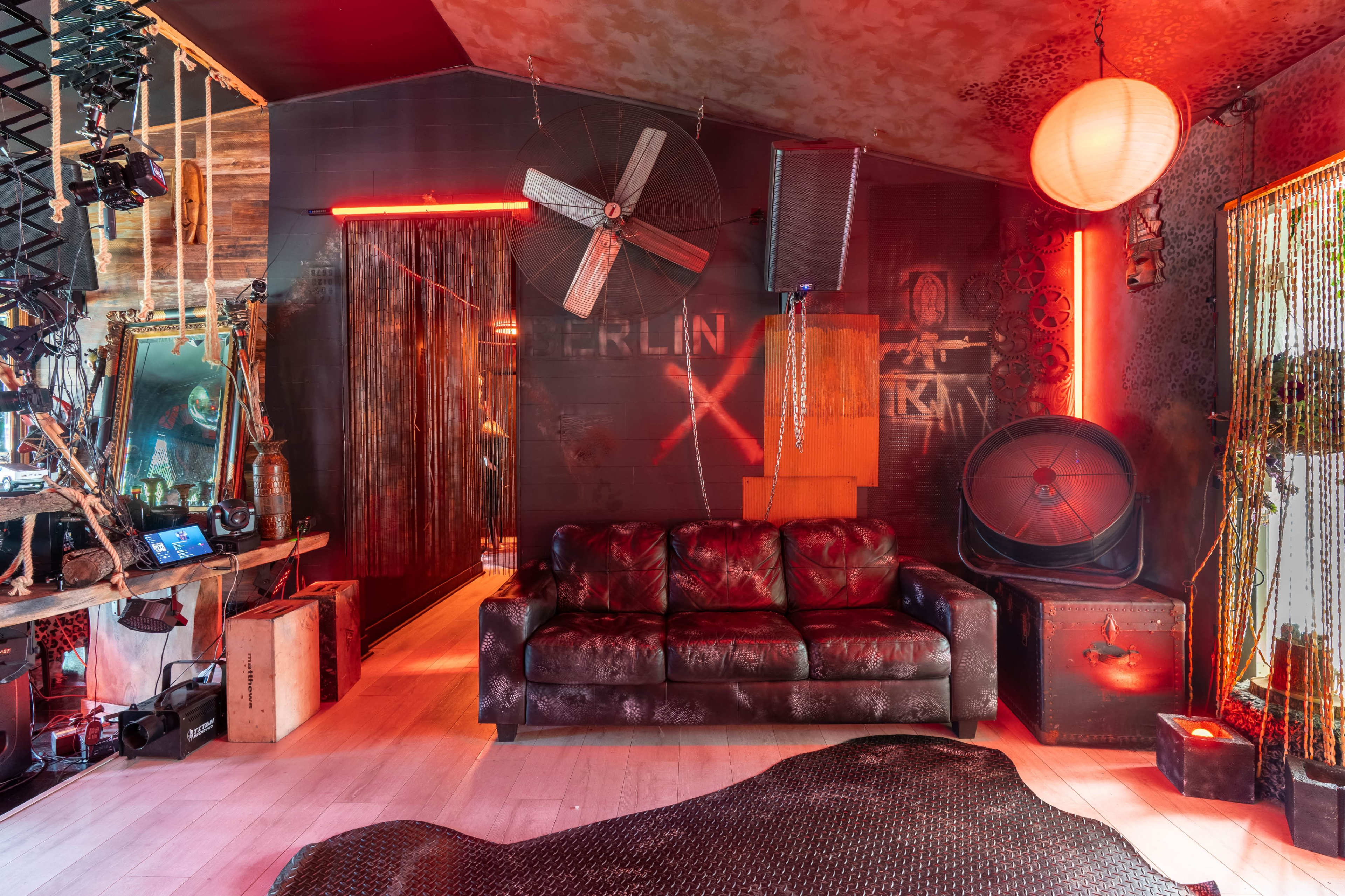 The room features a dark-themed interior with a leather sofa, industrial decor elements, and red lighting creating a moody atmosphere.