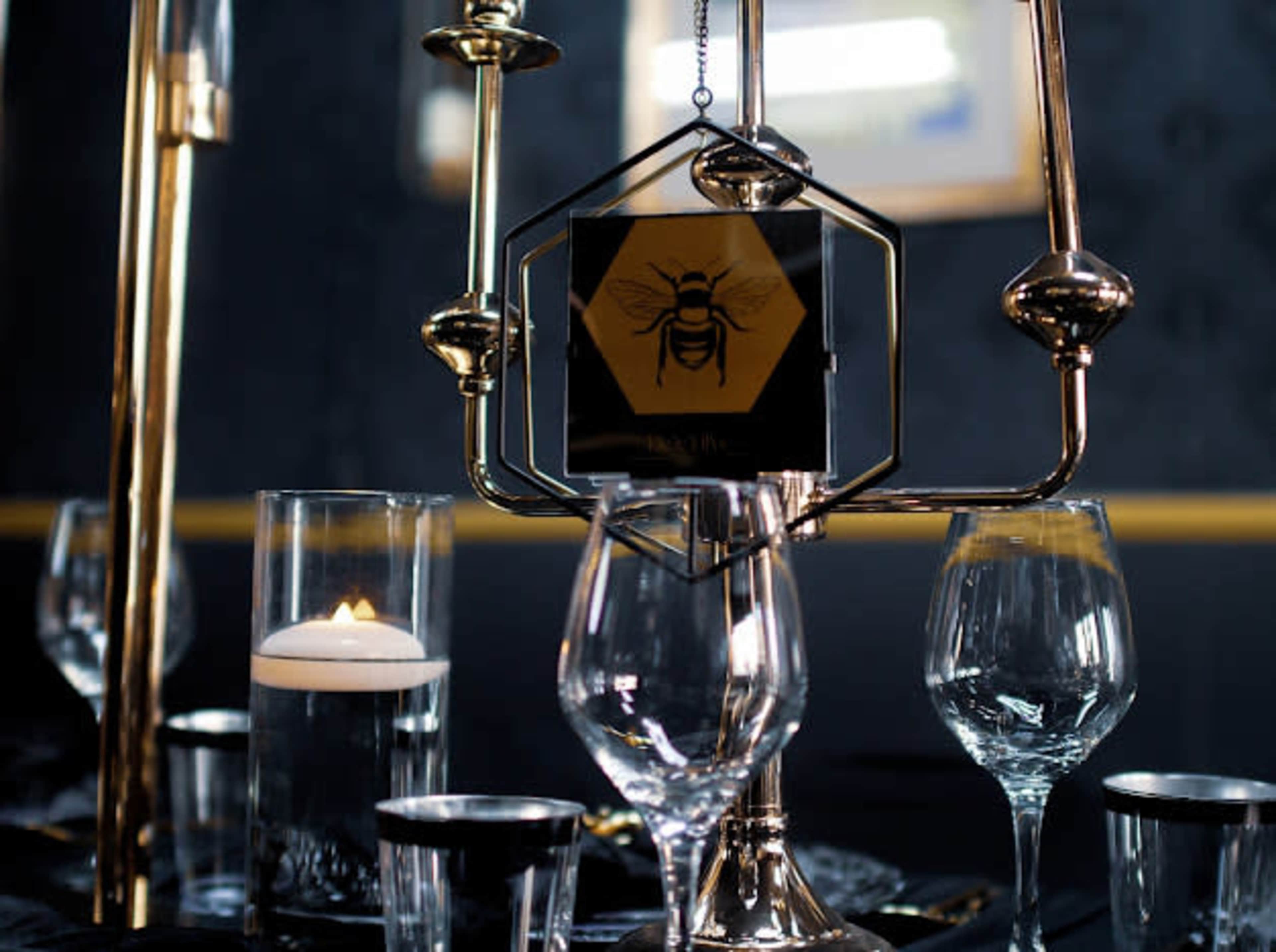 The image features an elegantly set dining table with a metallic centerpiece, a candle in a glass holder, and various glassware arranged around it.