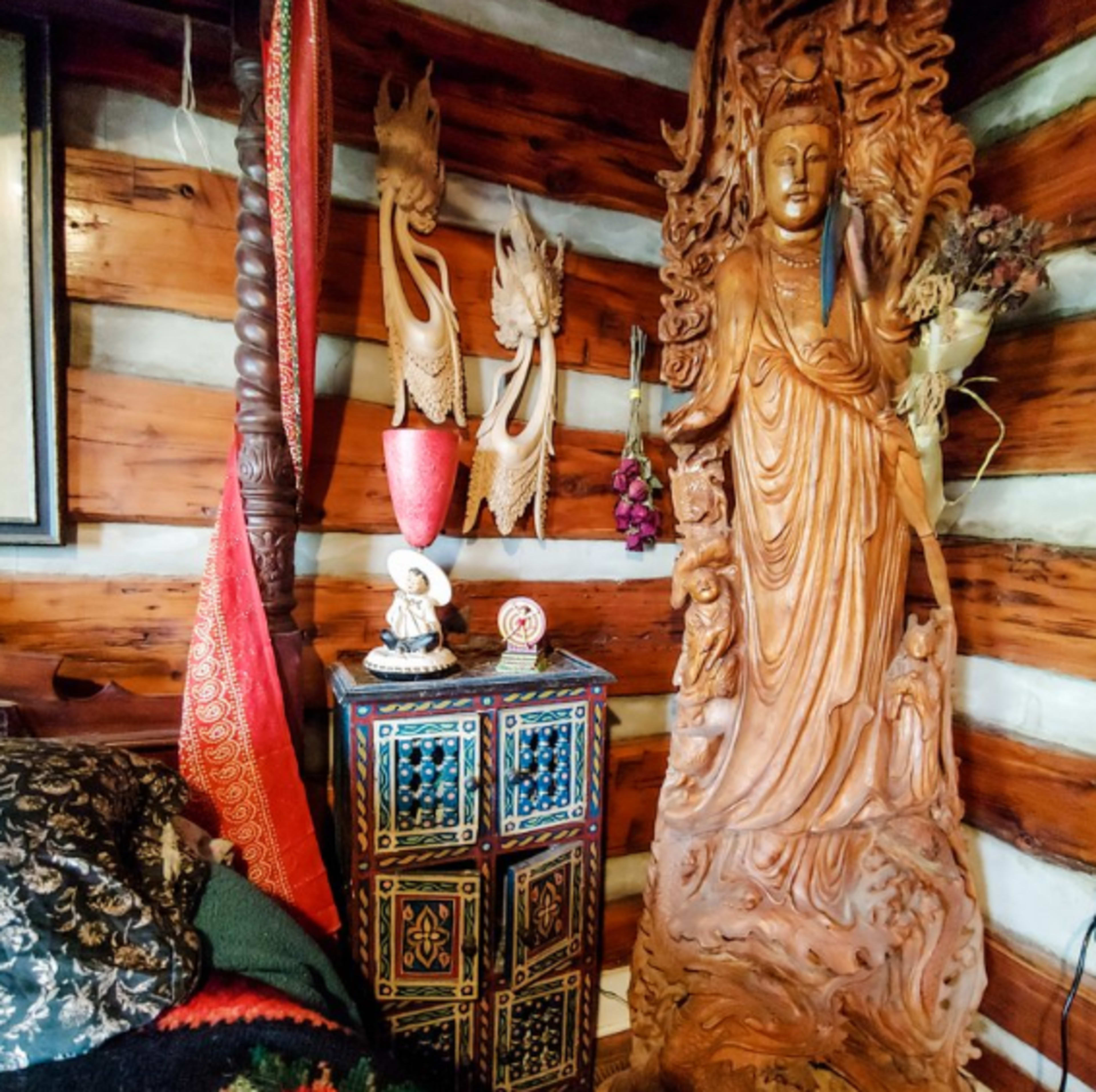 A wooden statue of a figure, likely a deity, next to a colorful, intricately designed cabinet in a room with wooden walls and various decorative items.