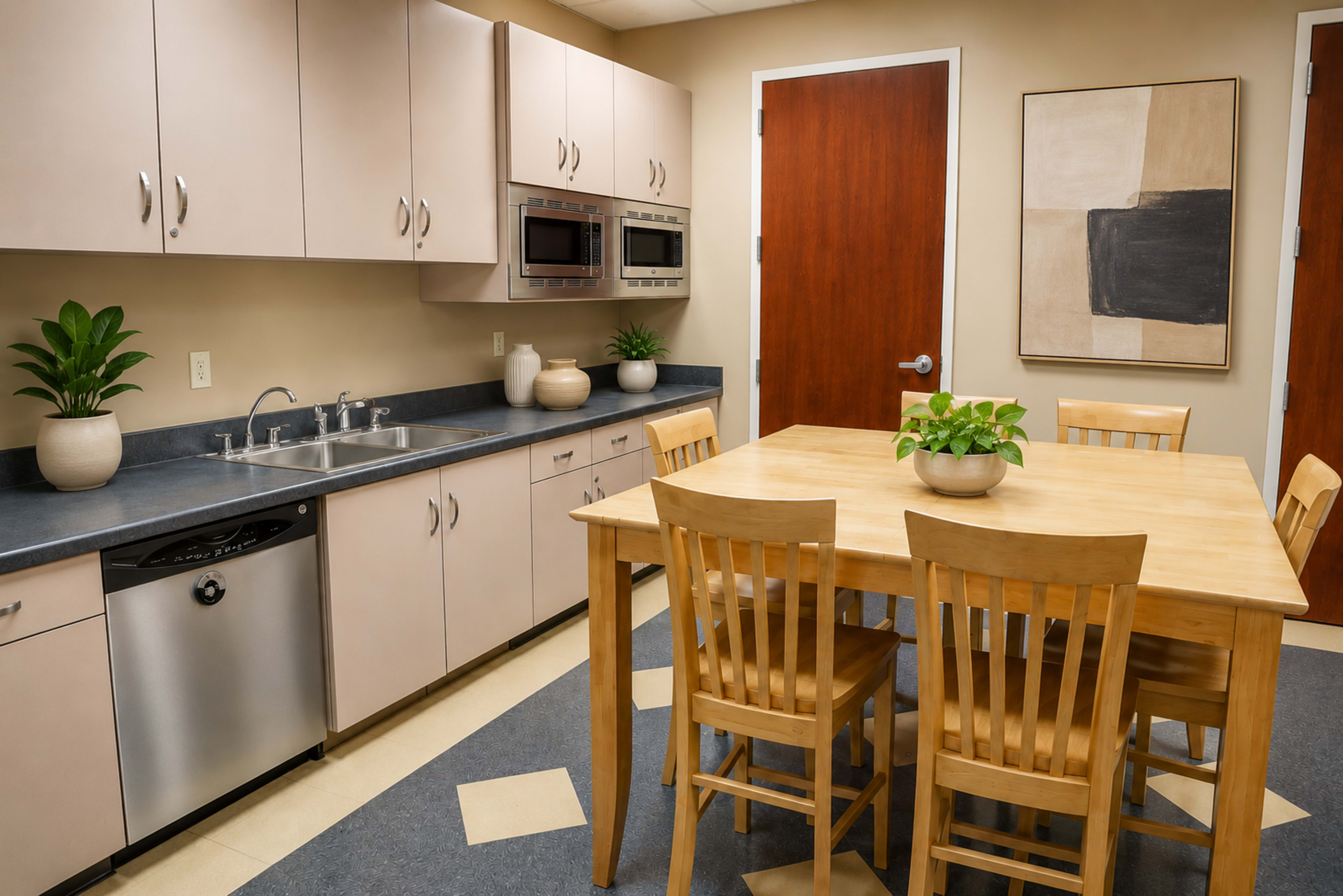 A modern kitchen features light cabinetry, stainless steel appliances, a wooden dining table with six chairs, and a door leading to another room.