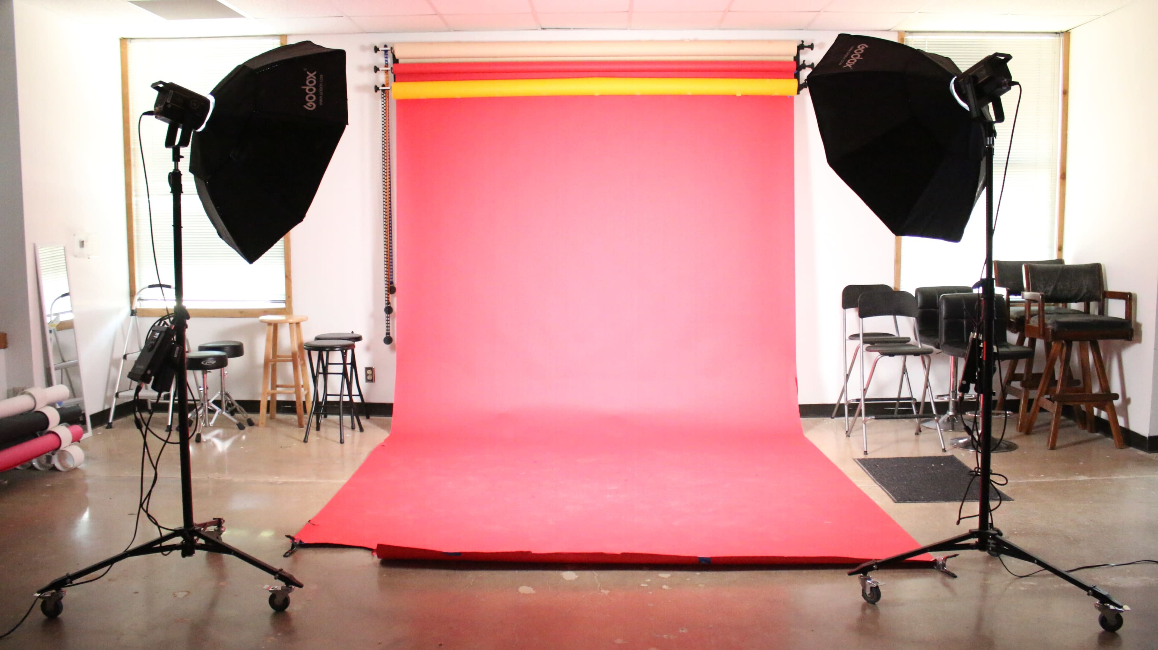 A photography studio setup with a pink backdrop and two softbox lights on either side.