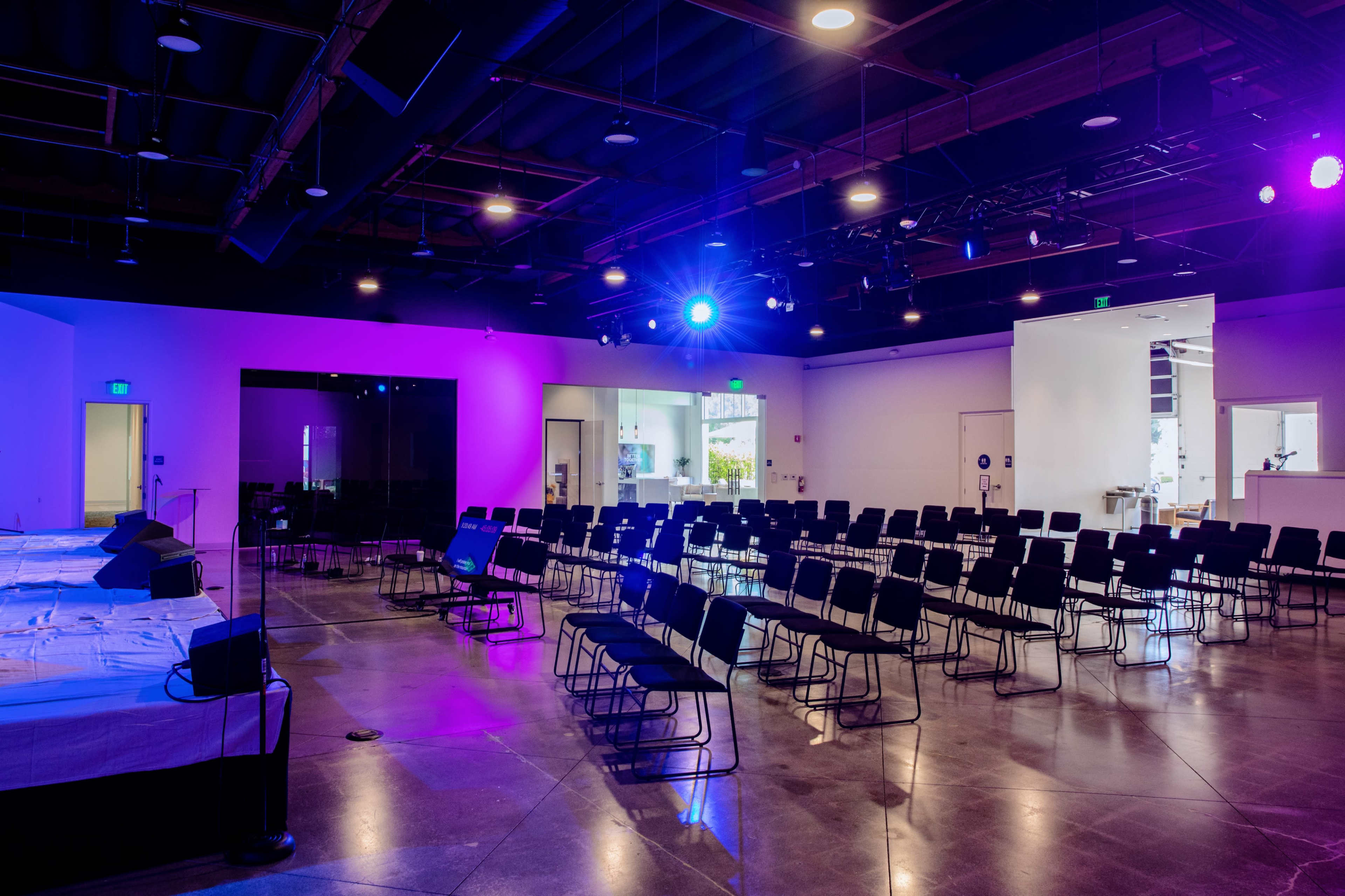 A spacious room with rows of black chairs arranged in a semi-circle, illuminated by colorful stage lighting.