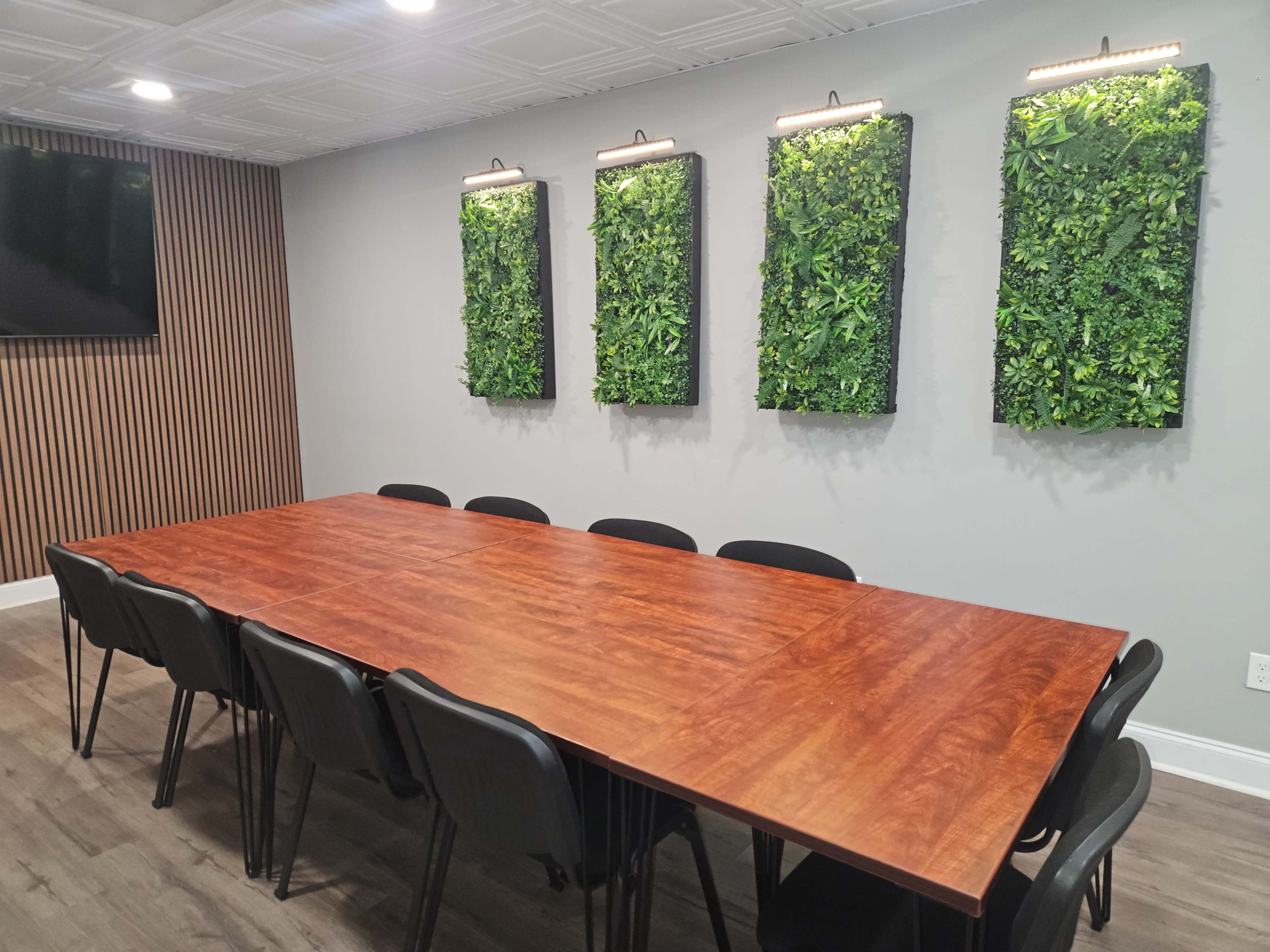 A long wooden conference table is surrounded by black chairs in a meeting room with green vertical gardens on the walls.