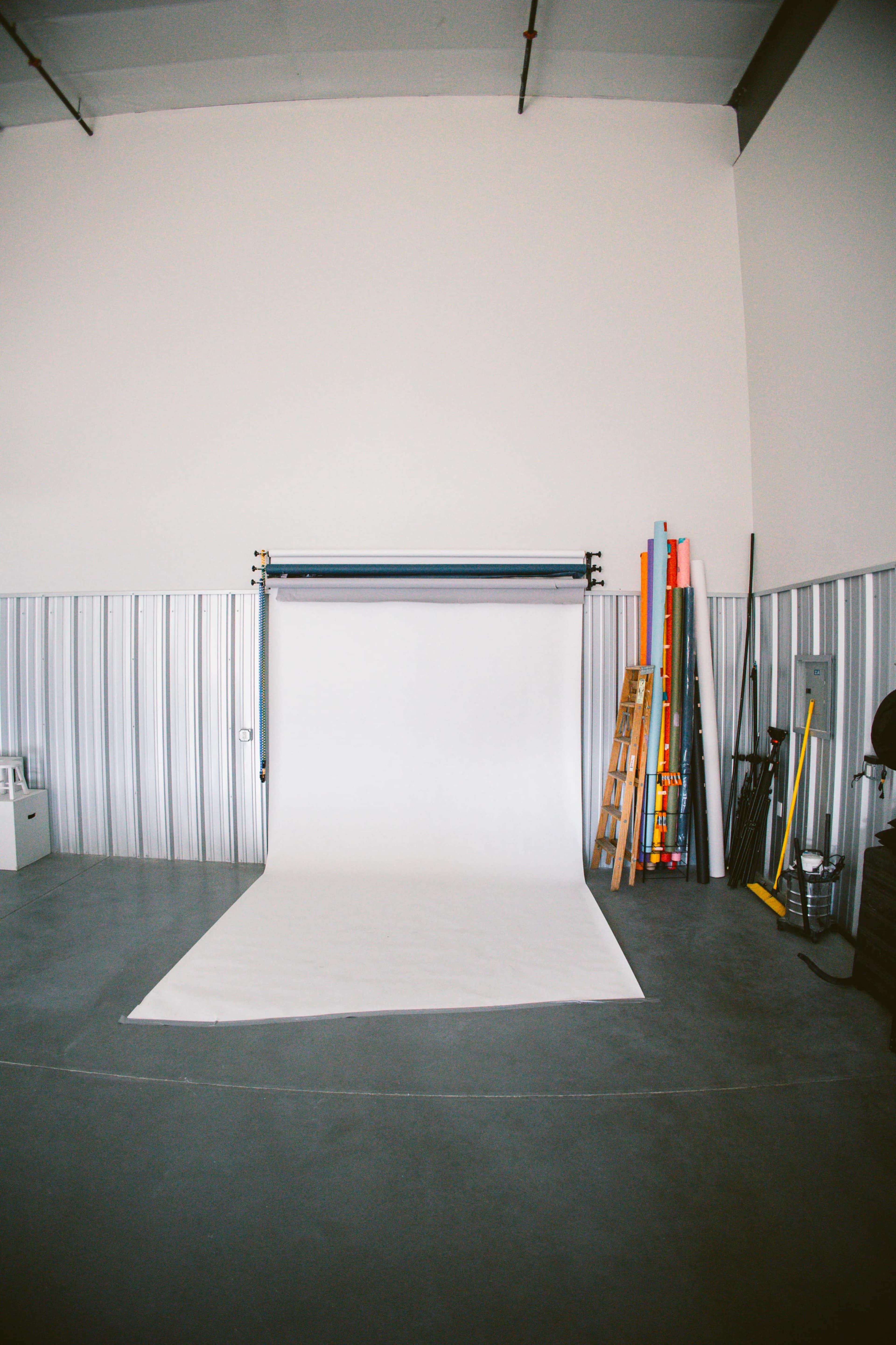 A photography studio with a white backdrop set up against a plain wall, surrounded by various equipment and props.