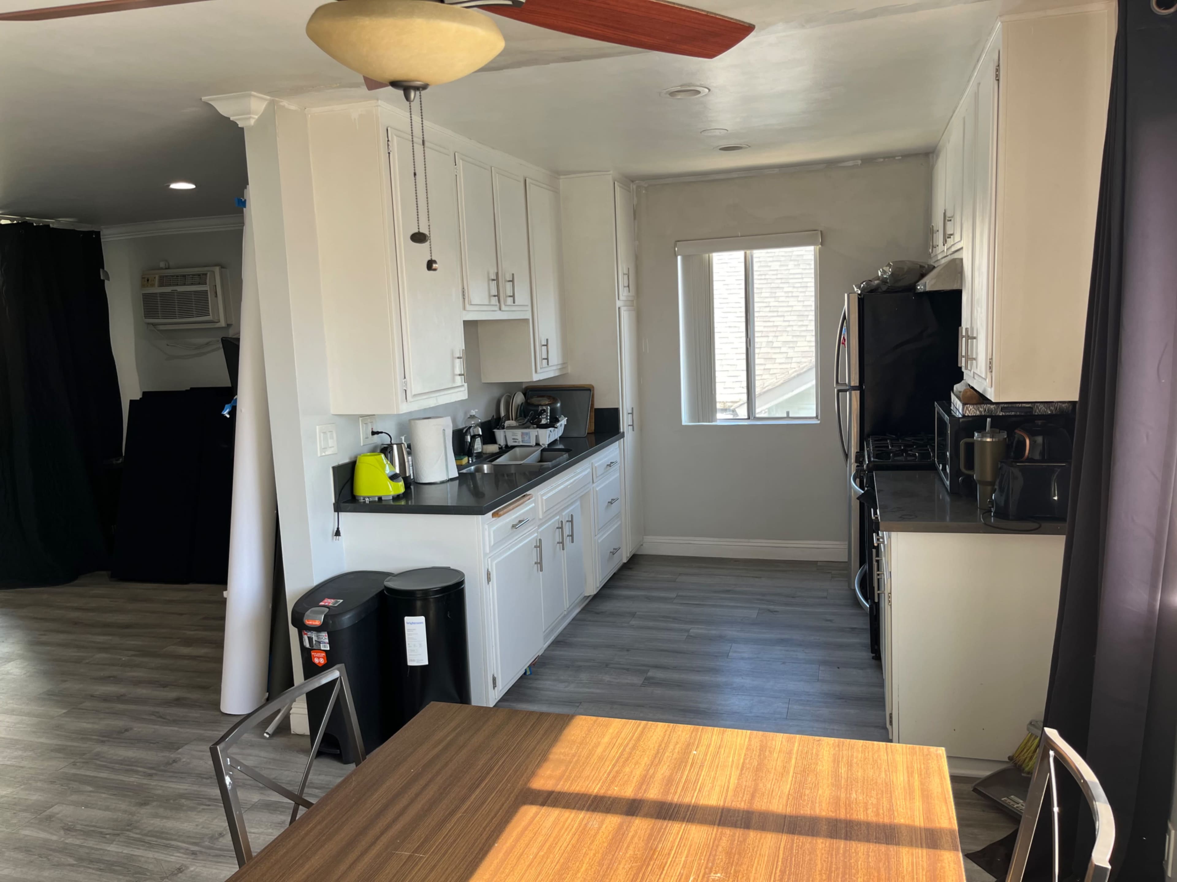 The image shows a modern kitchen with white cabinets, a black stove, and a small dining table beside a window.