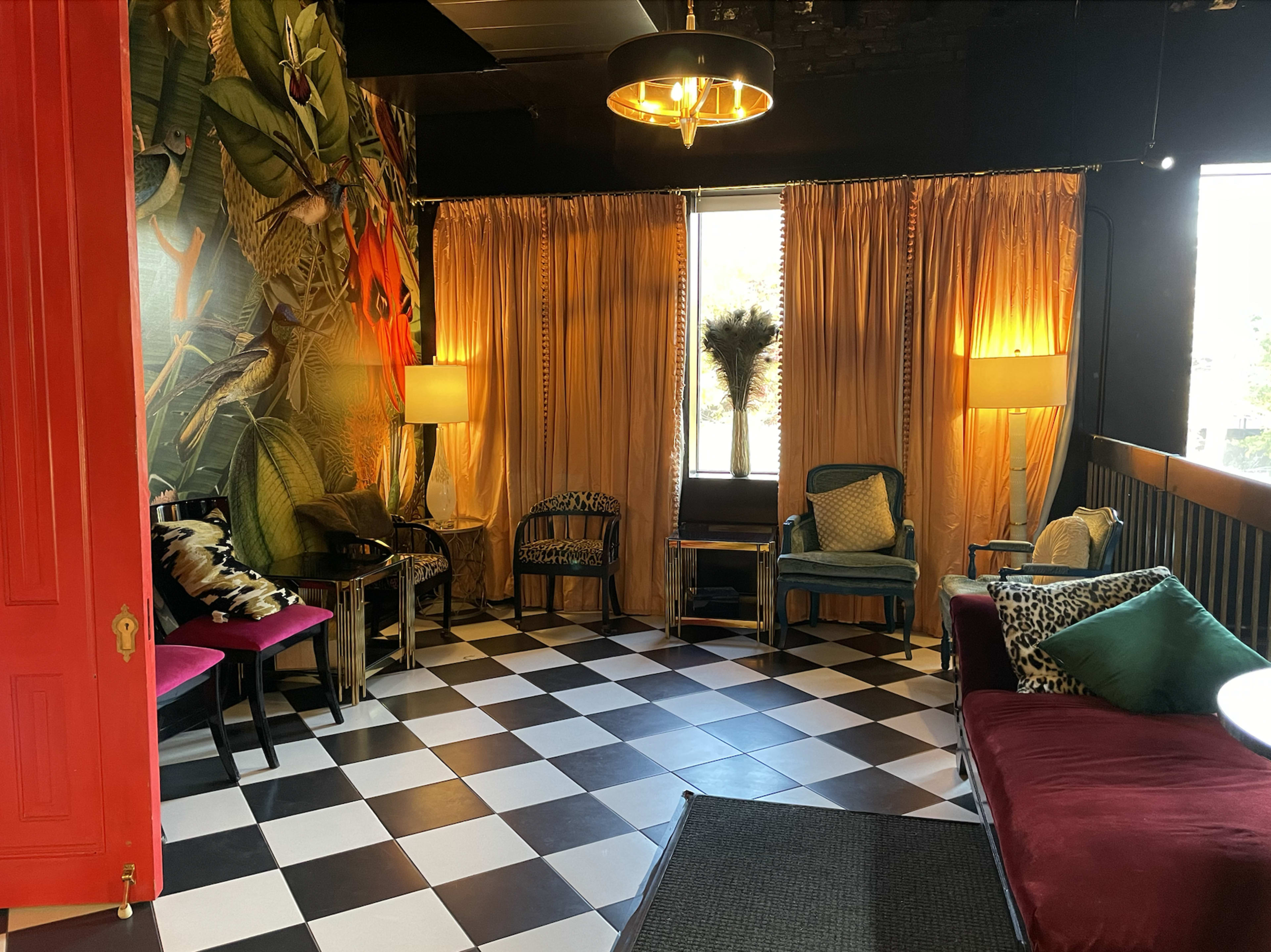 A seating area with a checkered floor, adorned with colorful curtains and various upholstered chairs.