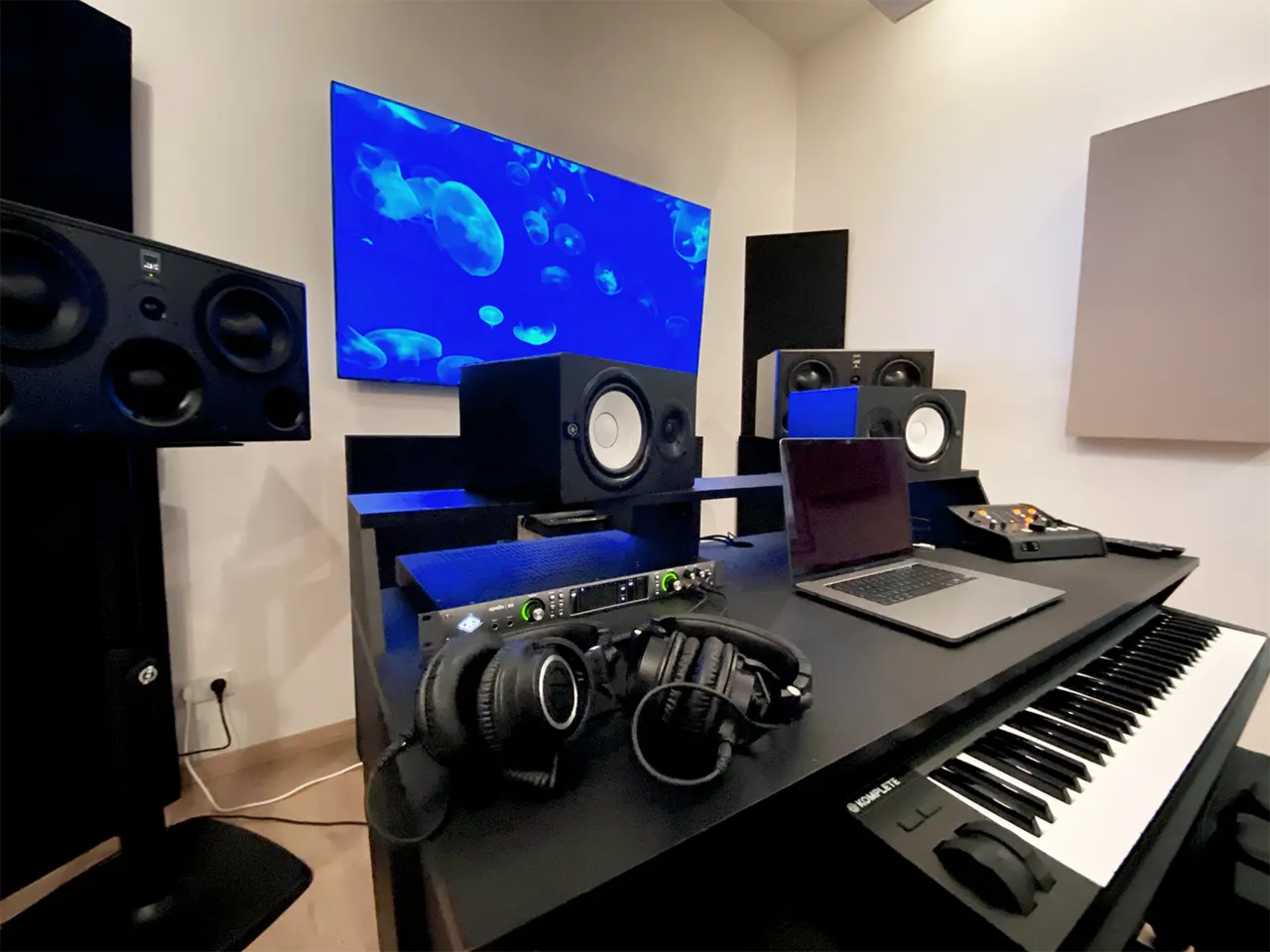 A modern music studio setup features multiple speakers, a laptop, headphones, and a keyboard, with a large screen displaying jellyfish in the background.