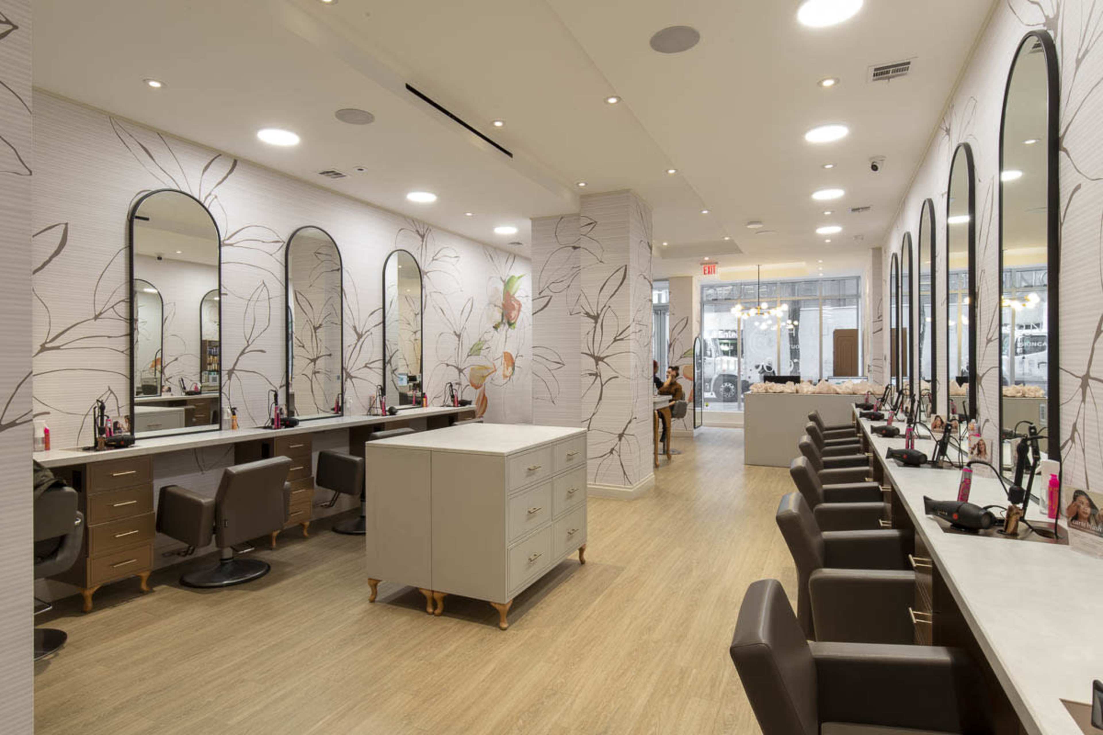 The image shows a modern salon interior featuring multiple styling stations with large mirrors, a central countertop, and a light wood floor.