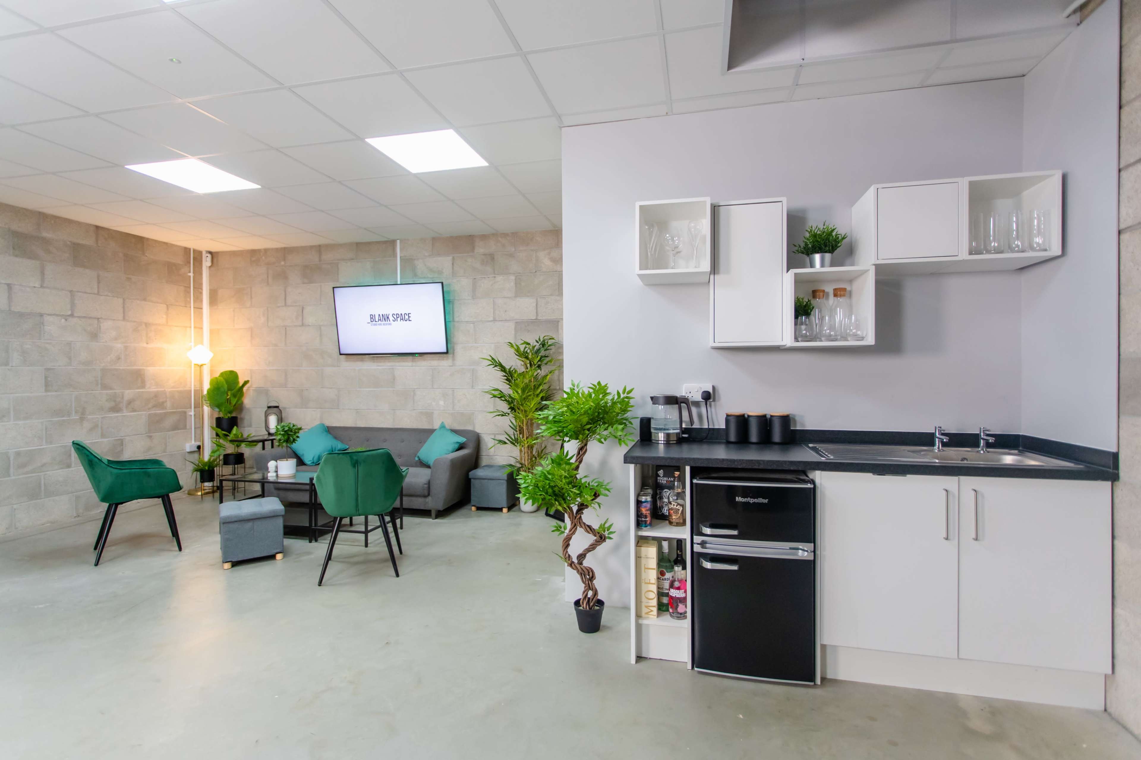 A modern office space featuring a kitchenette with a black countertop, a small dining area with chairs and a table, and a television mounted on the wall.