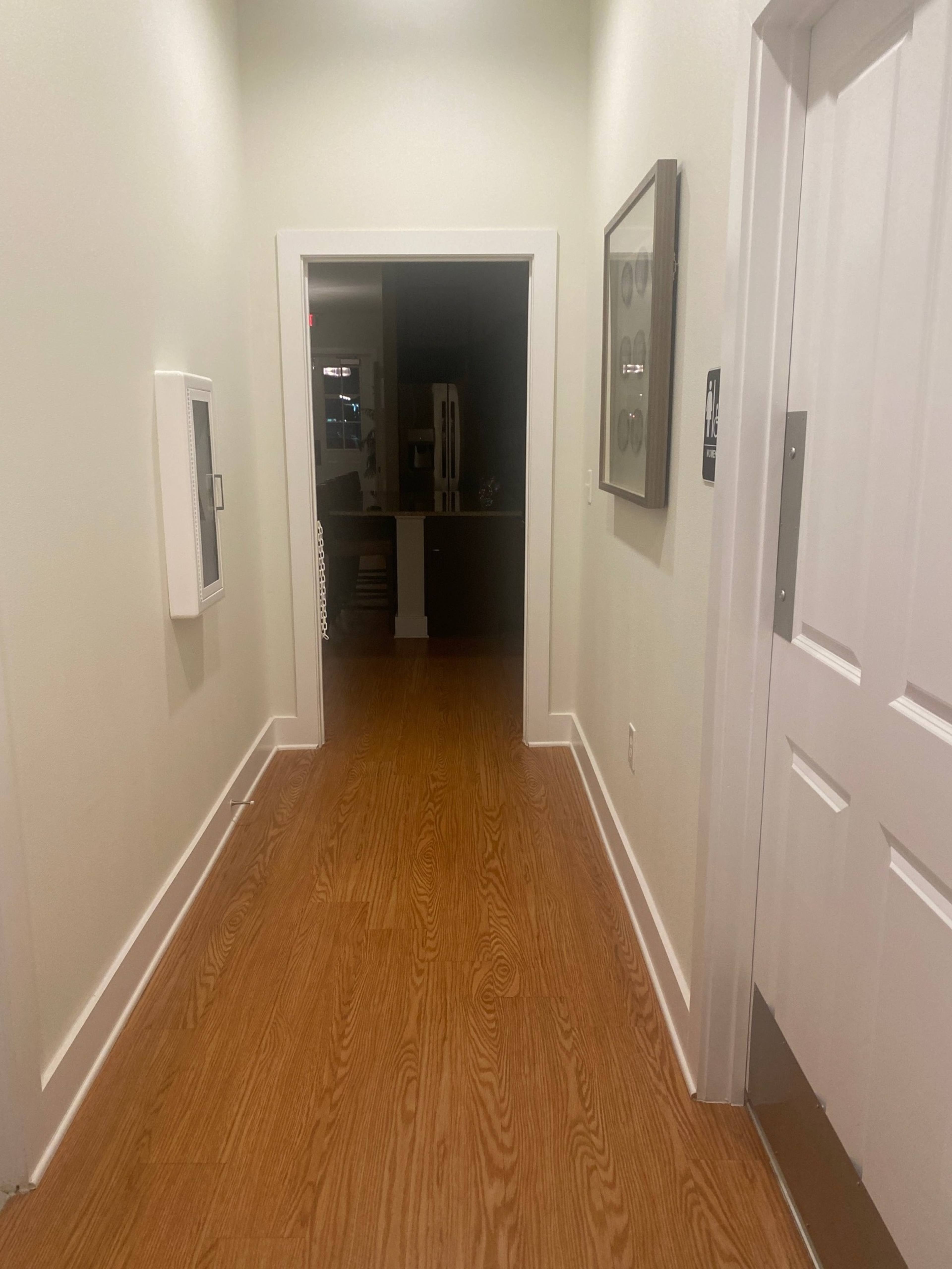 A narrow hallway with wooden flooring leads to an open doorway at the far end.