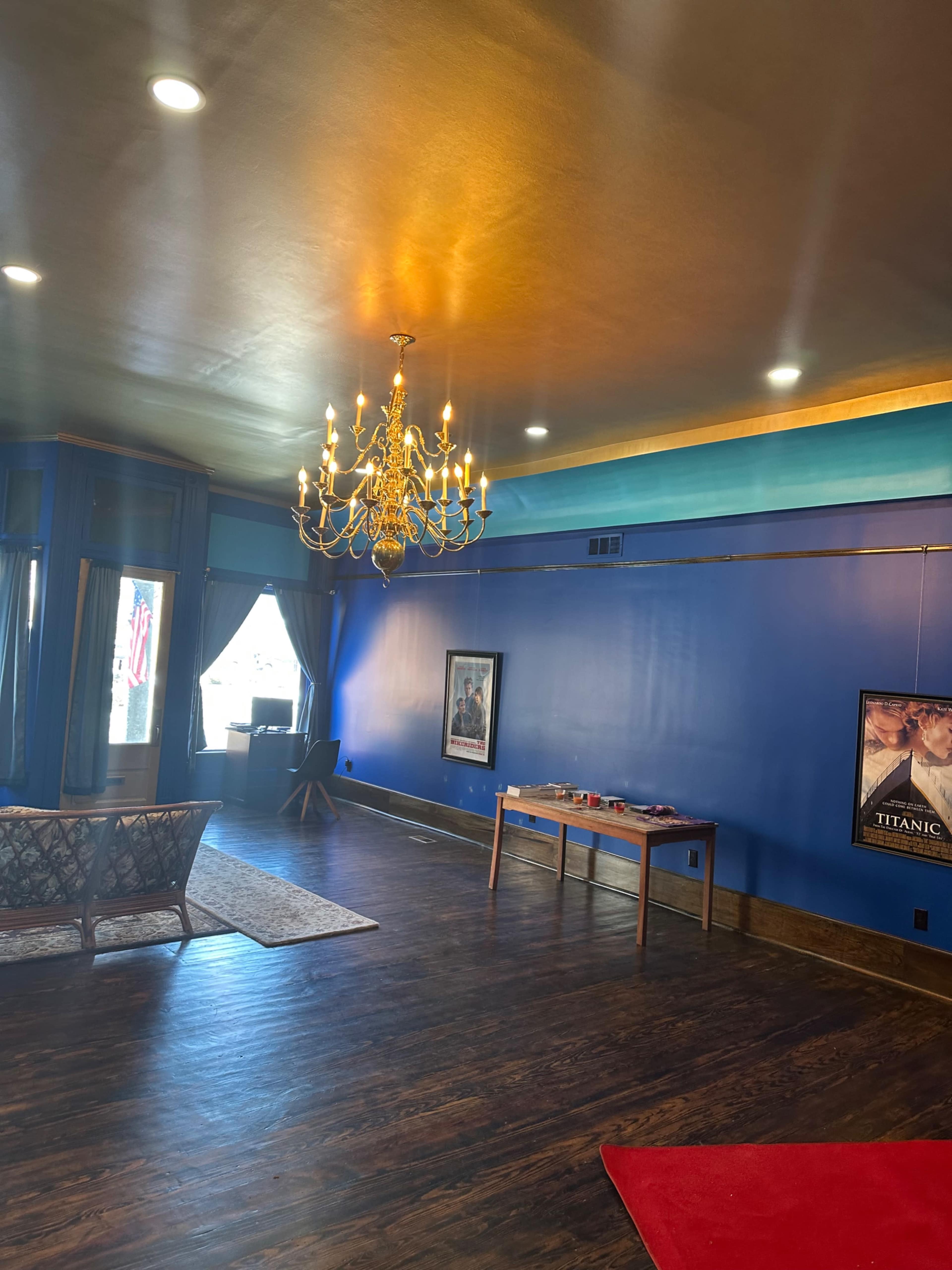 The room features blue walls, a chandelier, and a mix of decorative elements including a sofa, table, and a movie poster.