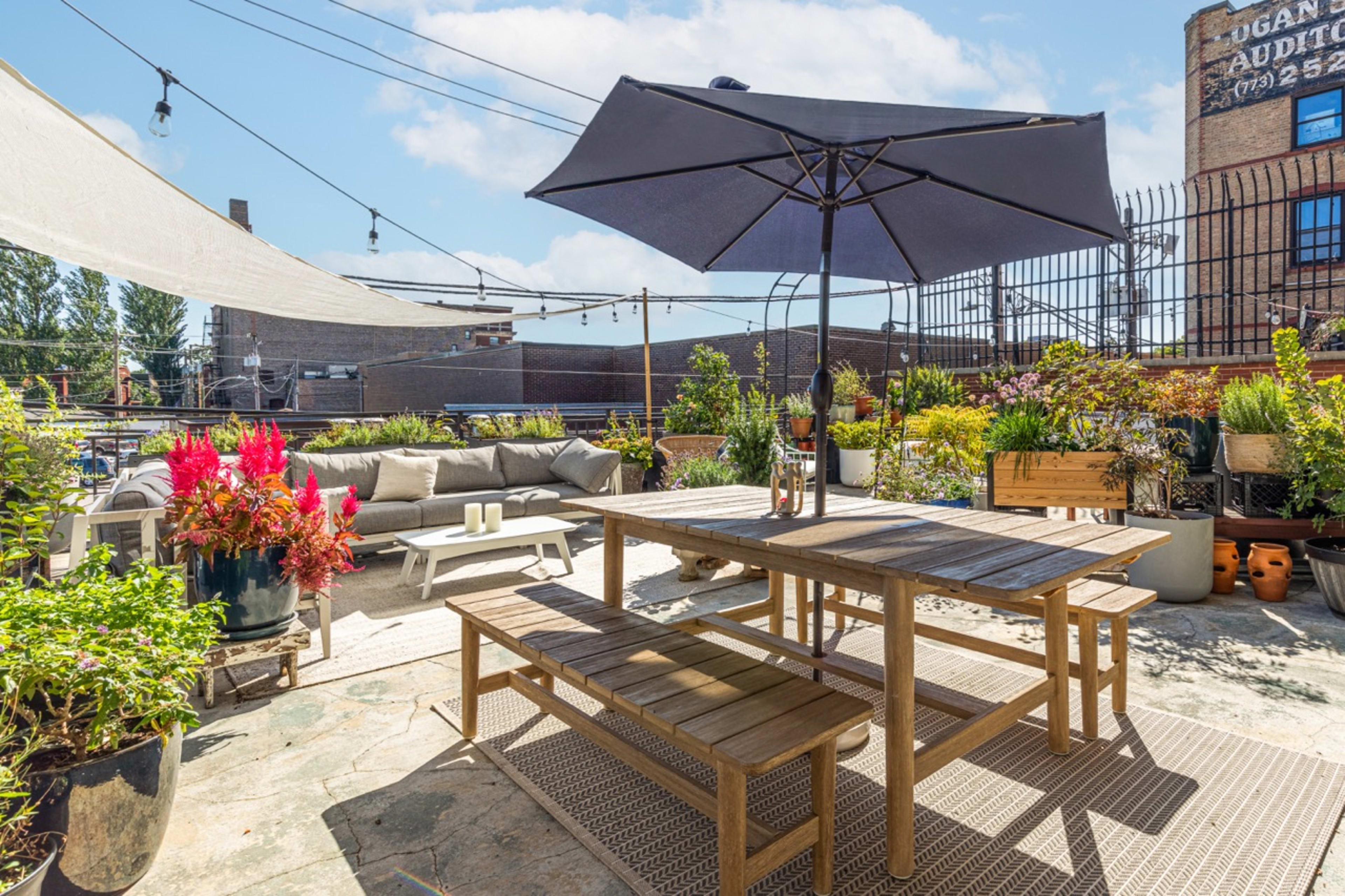A rooftop patio adorned with a wooden dining table, an umbrella, potted plants, and seating arranged for relaxation.