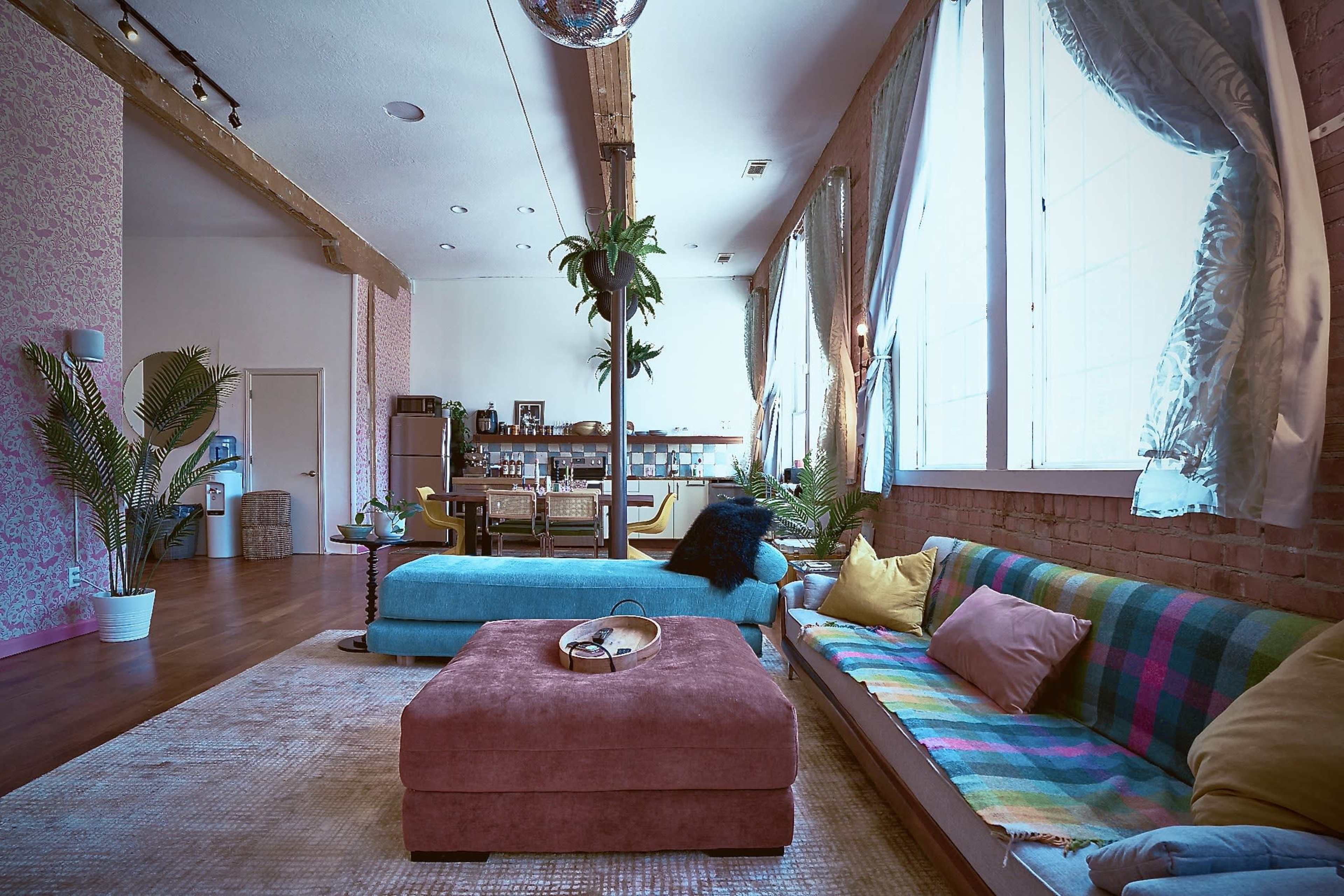 A spacious living area with a blue sofa, a pink ottoman, and large windows that allow natural light to fill the room.