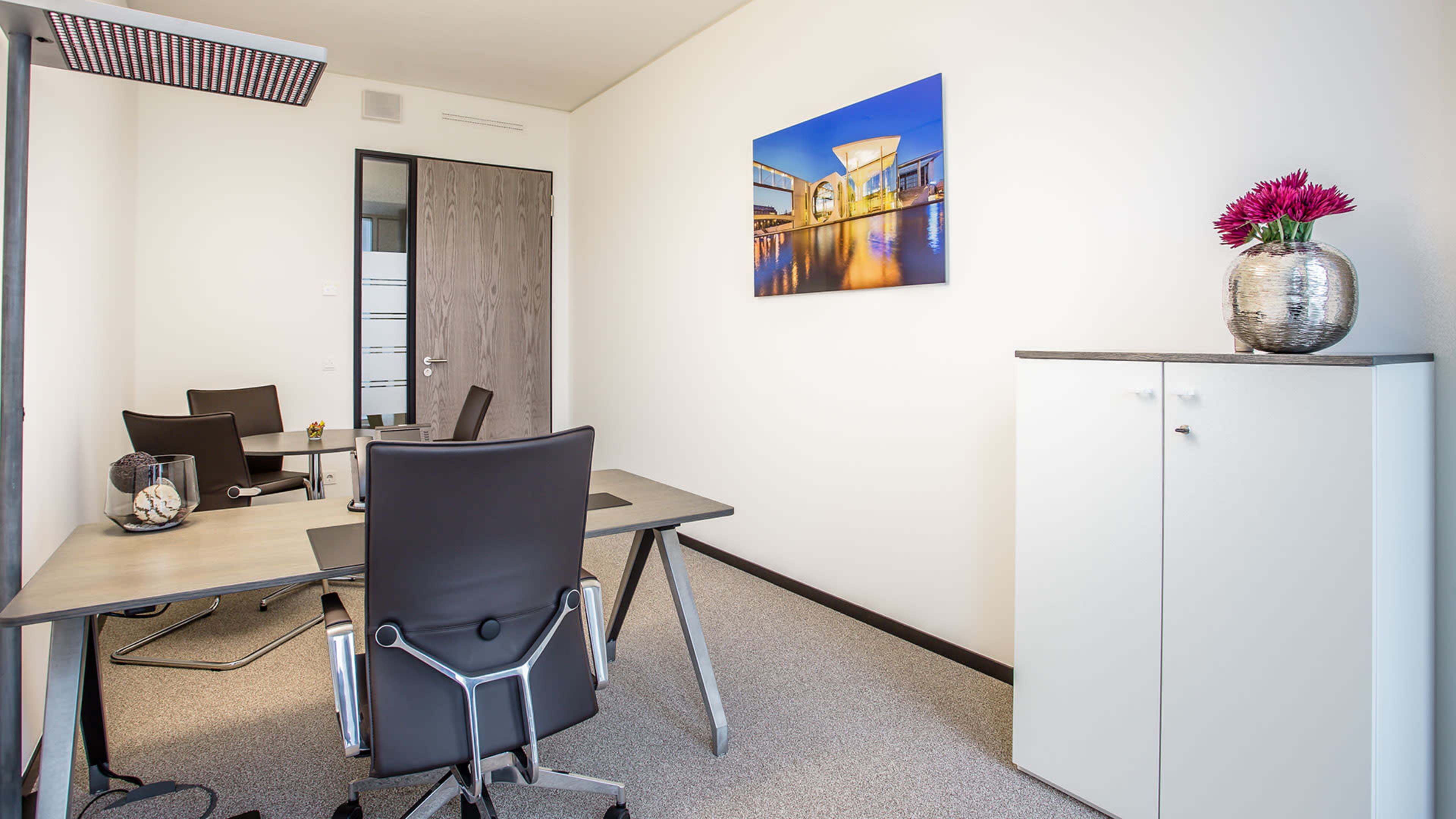 The image shows a modern office space featuring a desk, two chairs, a cabinet, and a large wall-mounted photograph.