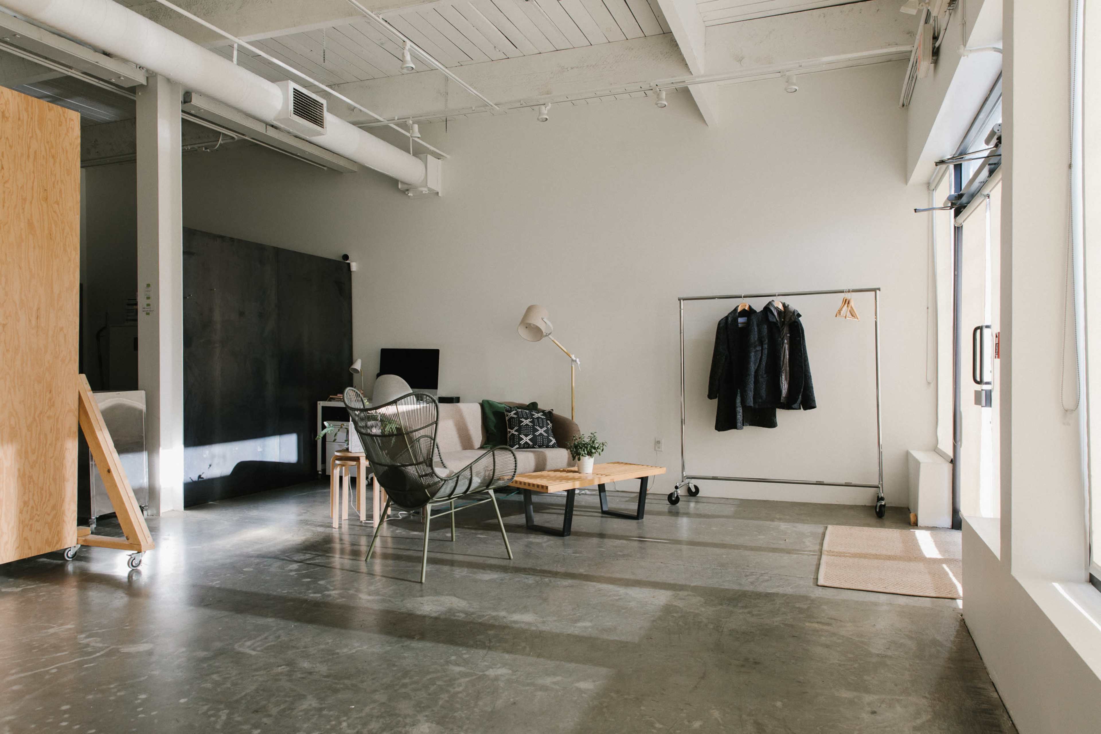 A modern, open-concept living space featuring a sofa, a coffee table, a floor lamp, and a coat rack against a light-colored wall.