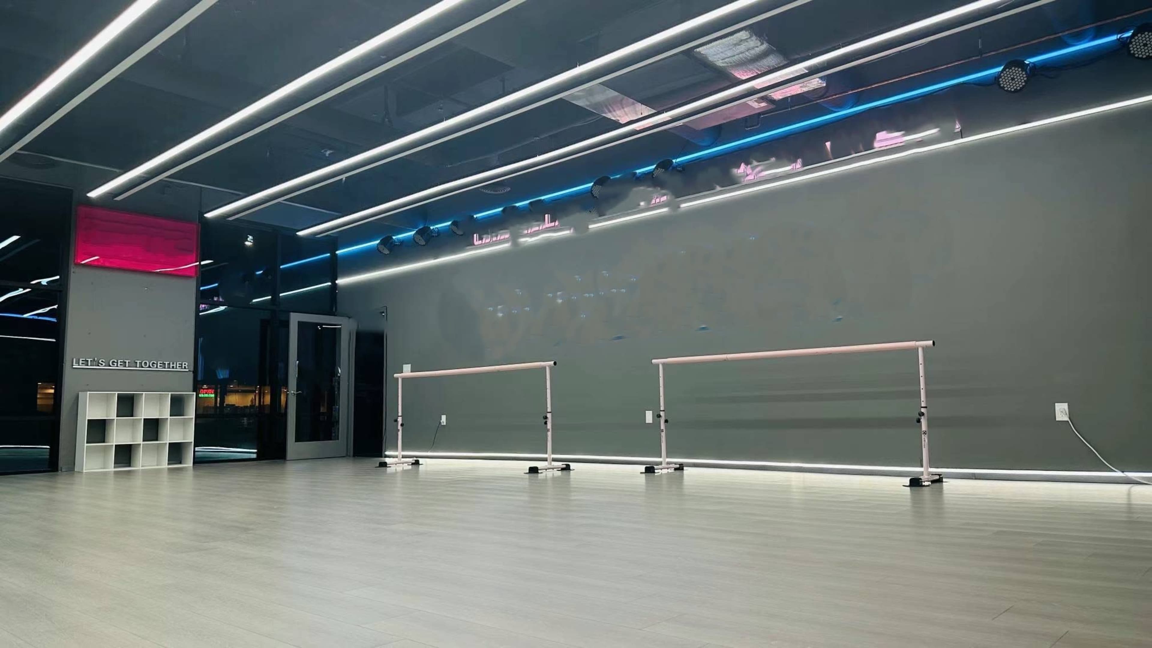 A spacious, brightly lit studio with mirrored walls and two ballet barres placed in the center against a grey backdrop.