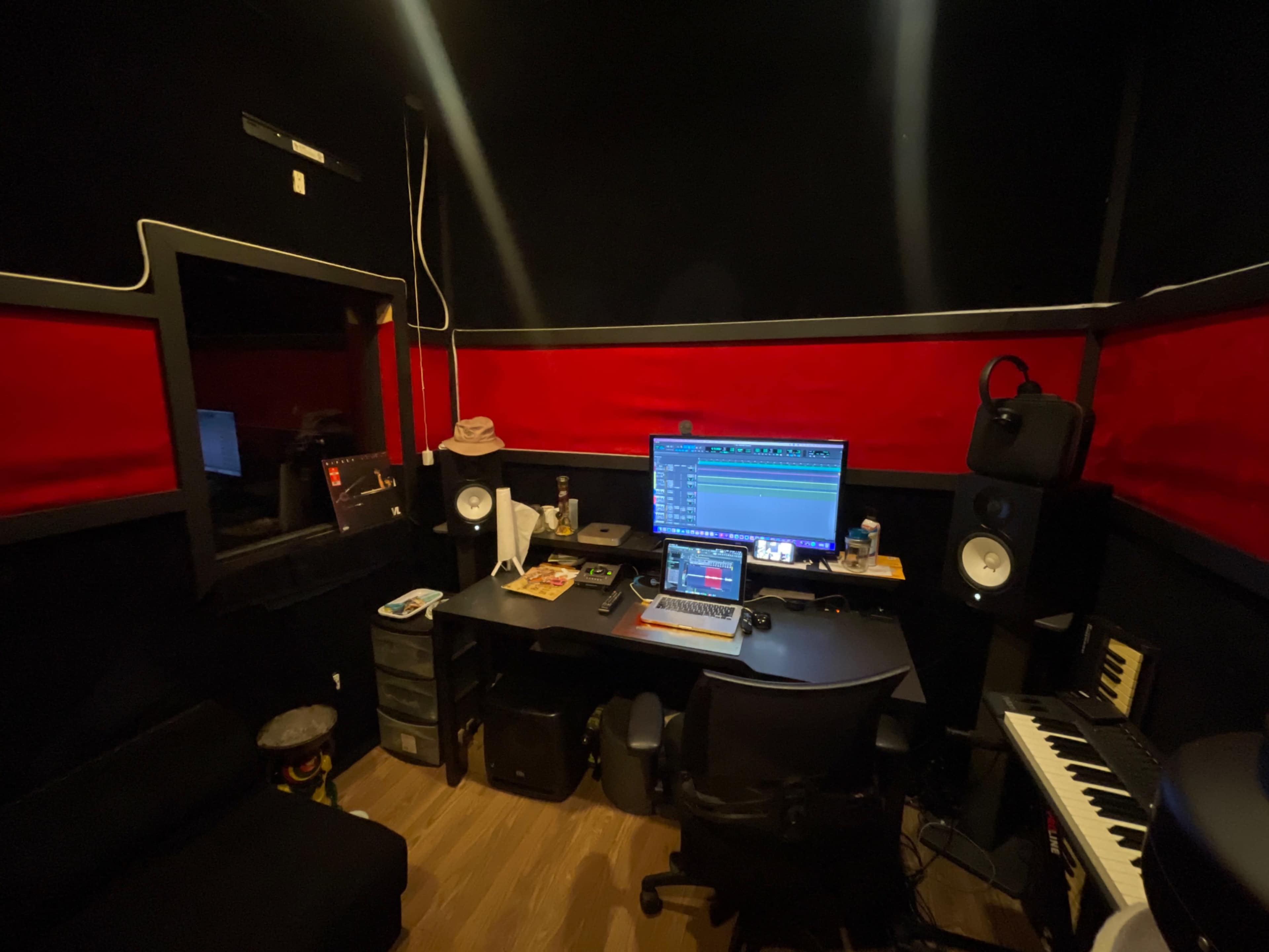 The image shows a recording studio setup featuring a computer workstation, audio monitors, a keyboard, and soundproofing elements.