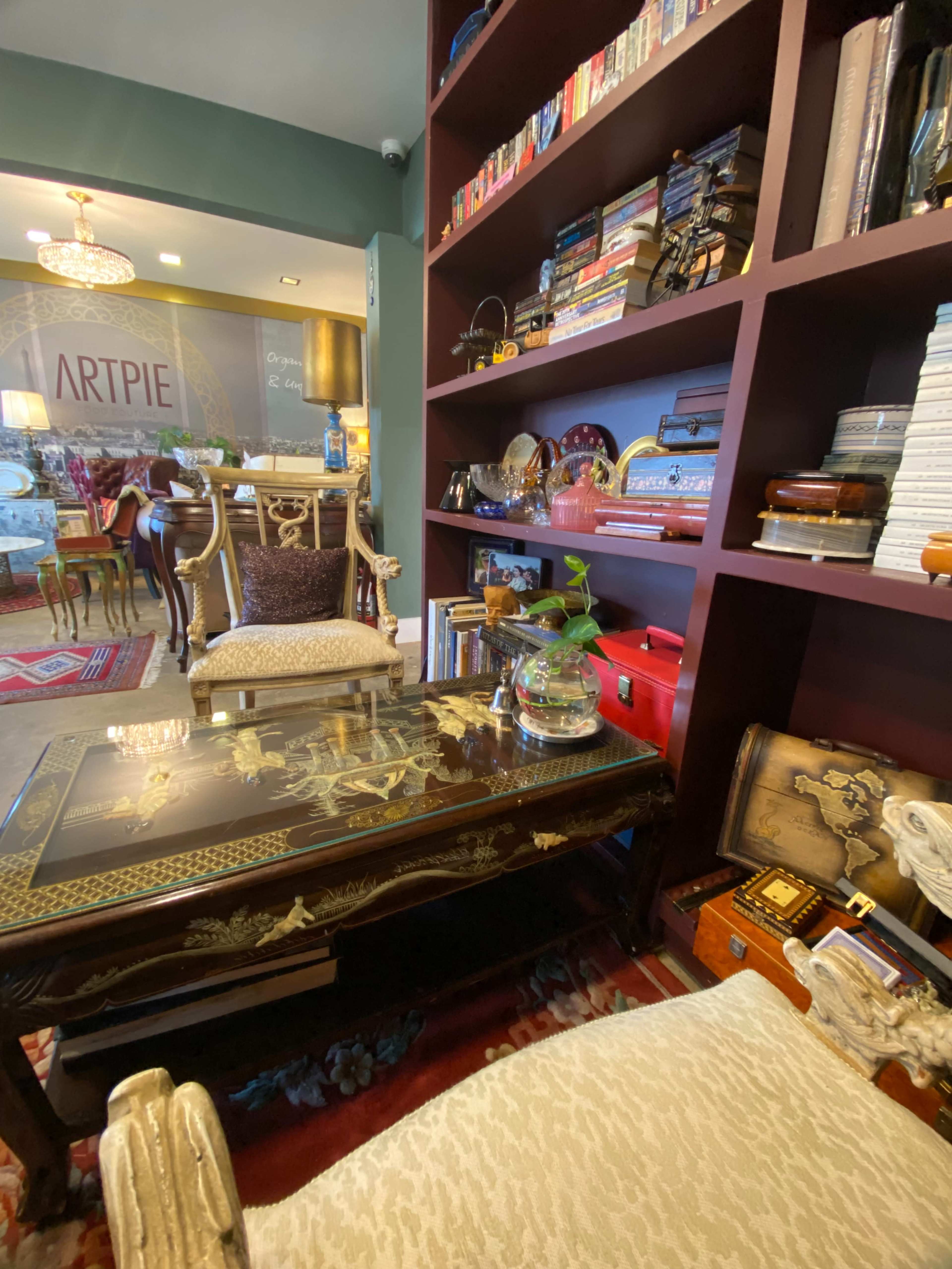 A cozy reading nook featuring a low table with intricate designs, two plush chairs, and a bookshelf filled with books and decorative items.