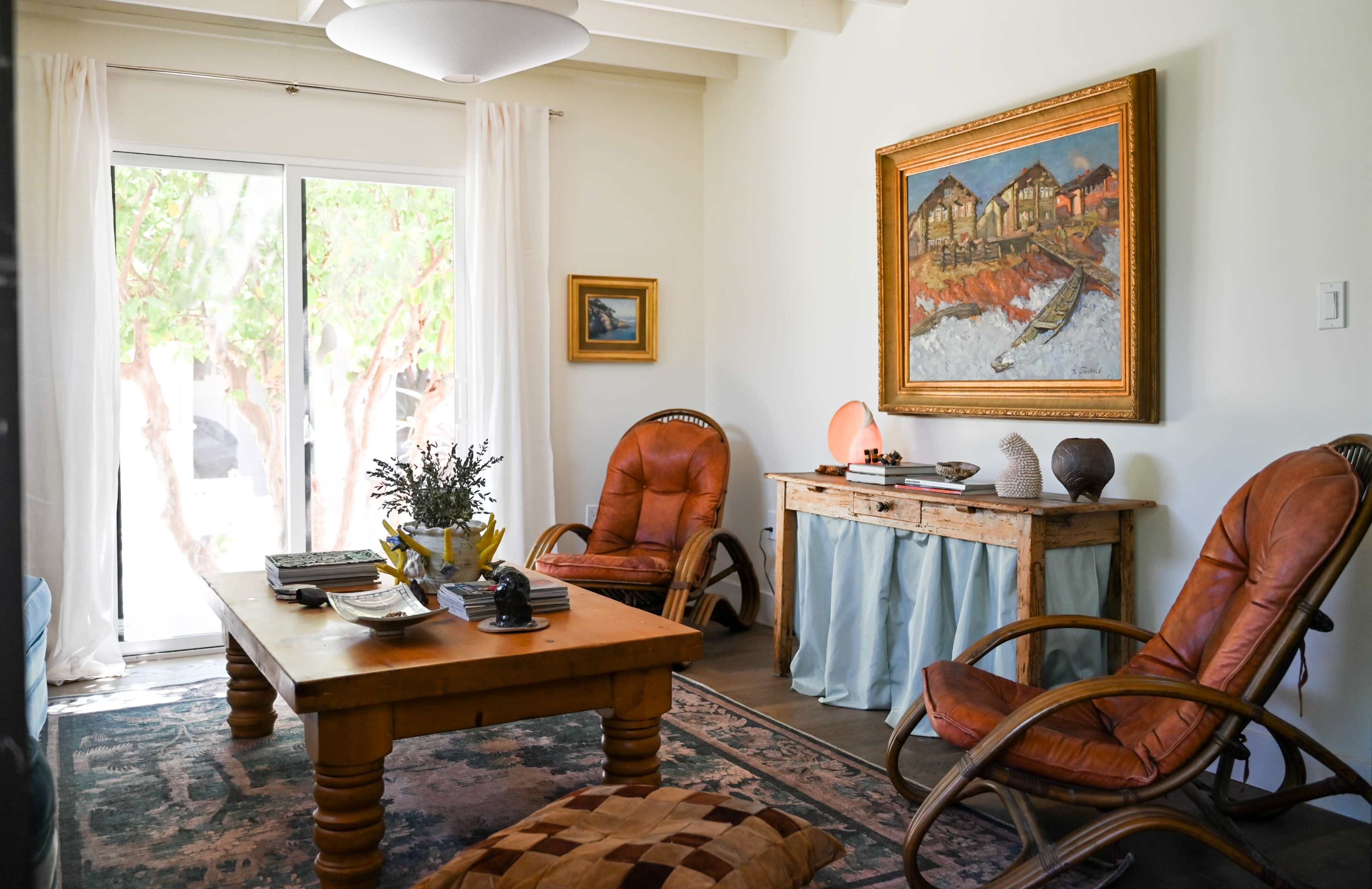 The living room features a wooden coffee table surrounded by two brown armchairs, with a large painting hanging above a wooden console table.