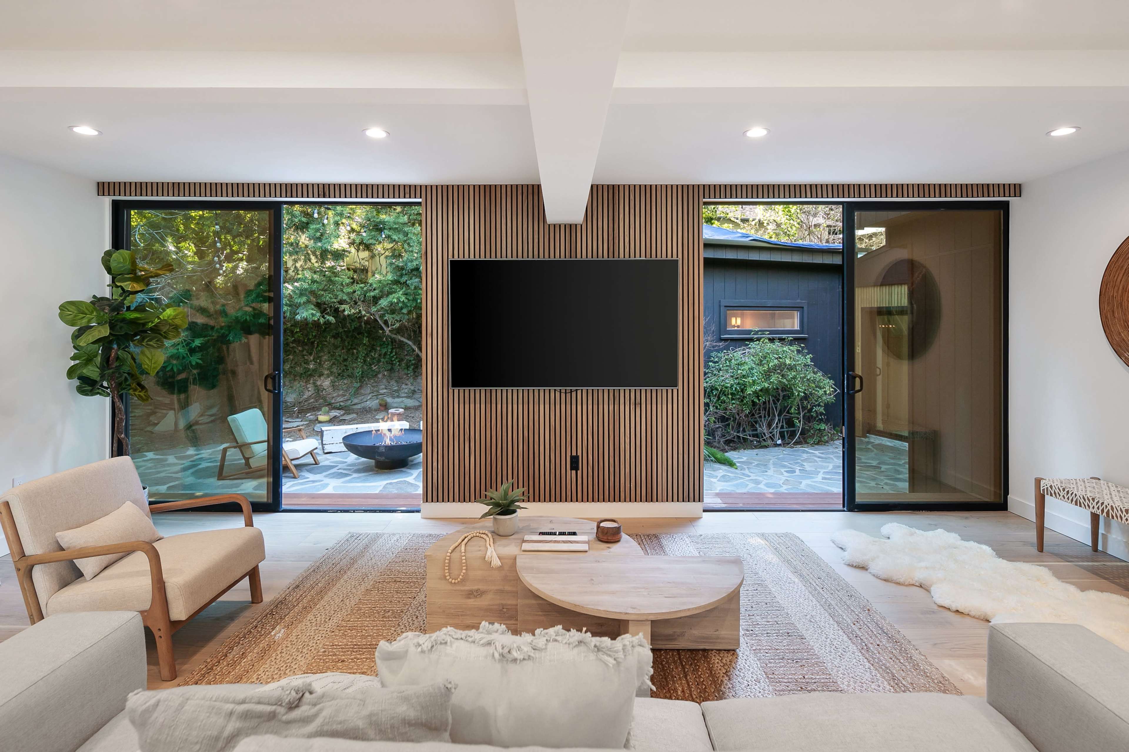 A modern living room features two large glass doors that open to a patio, with a neutral color scheme and minimalist furniture.