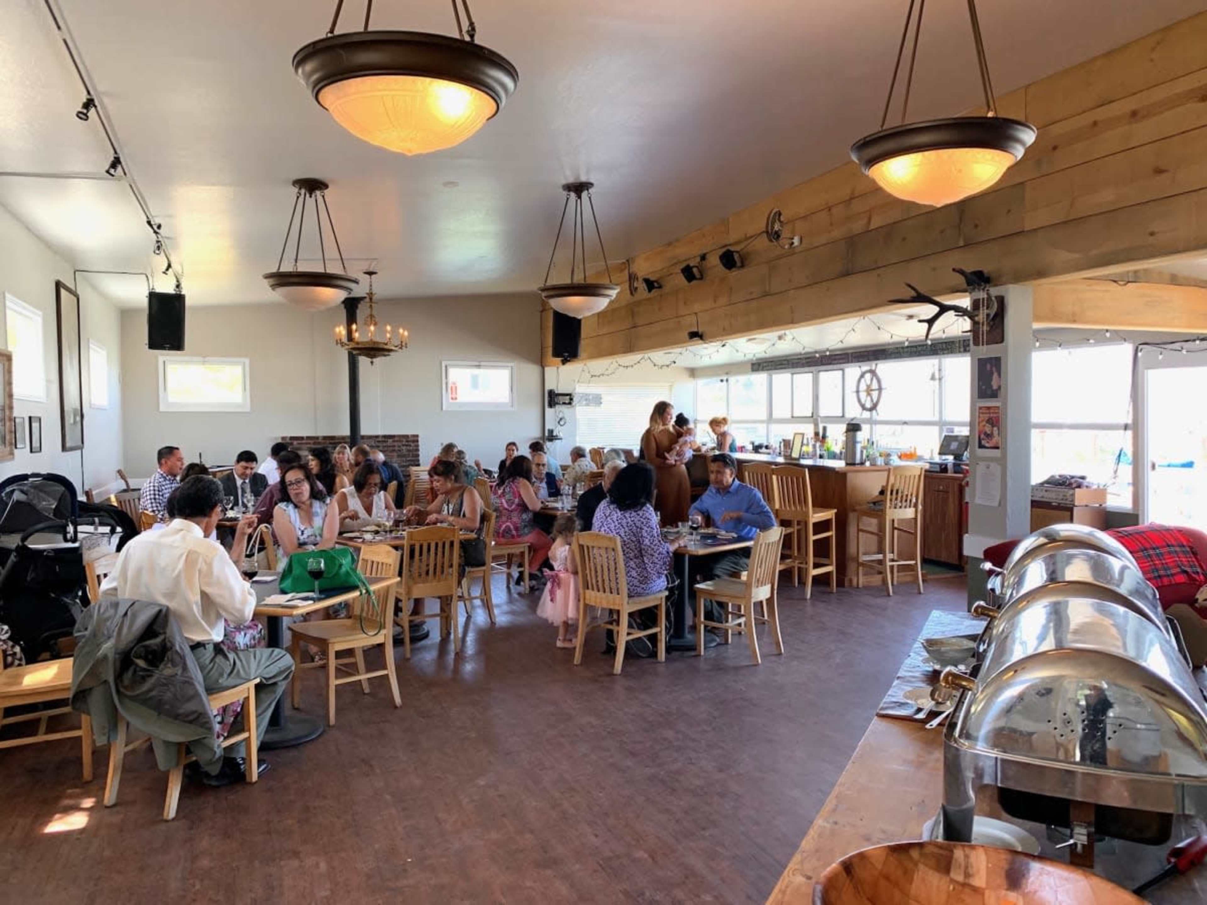 A busy indoor restaurant features various tables occupied by diners and a buffet area in the background.