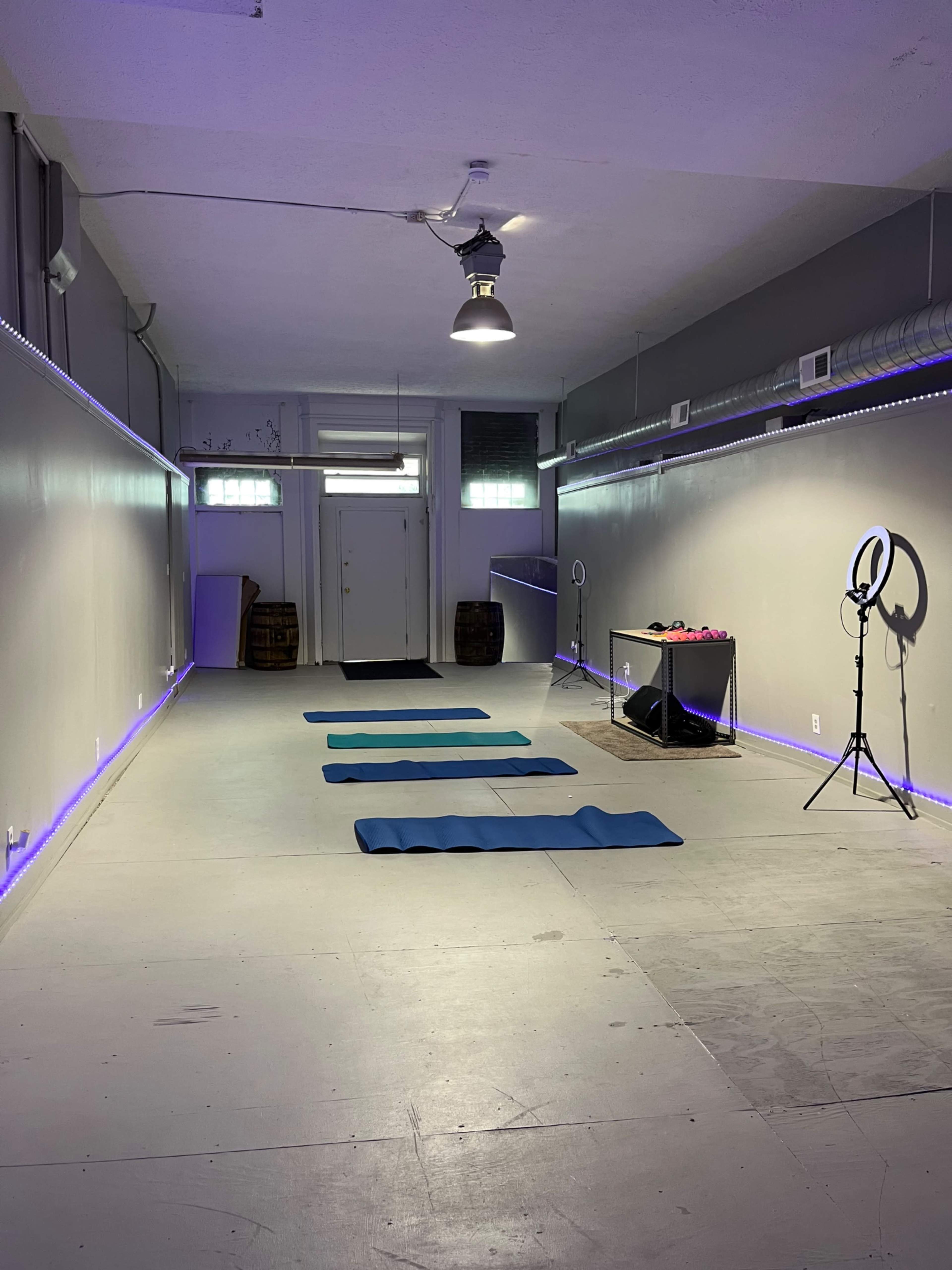 A spacious room designed for fitness or yoga with three blue exercise mats, a table with equipment, and a ring light.