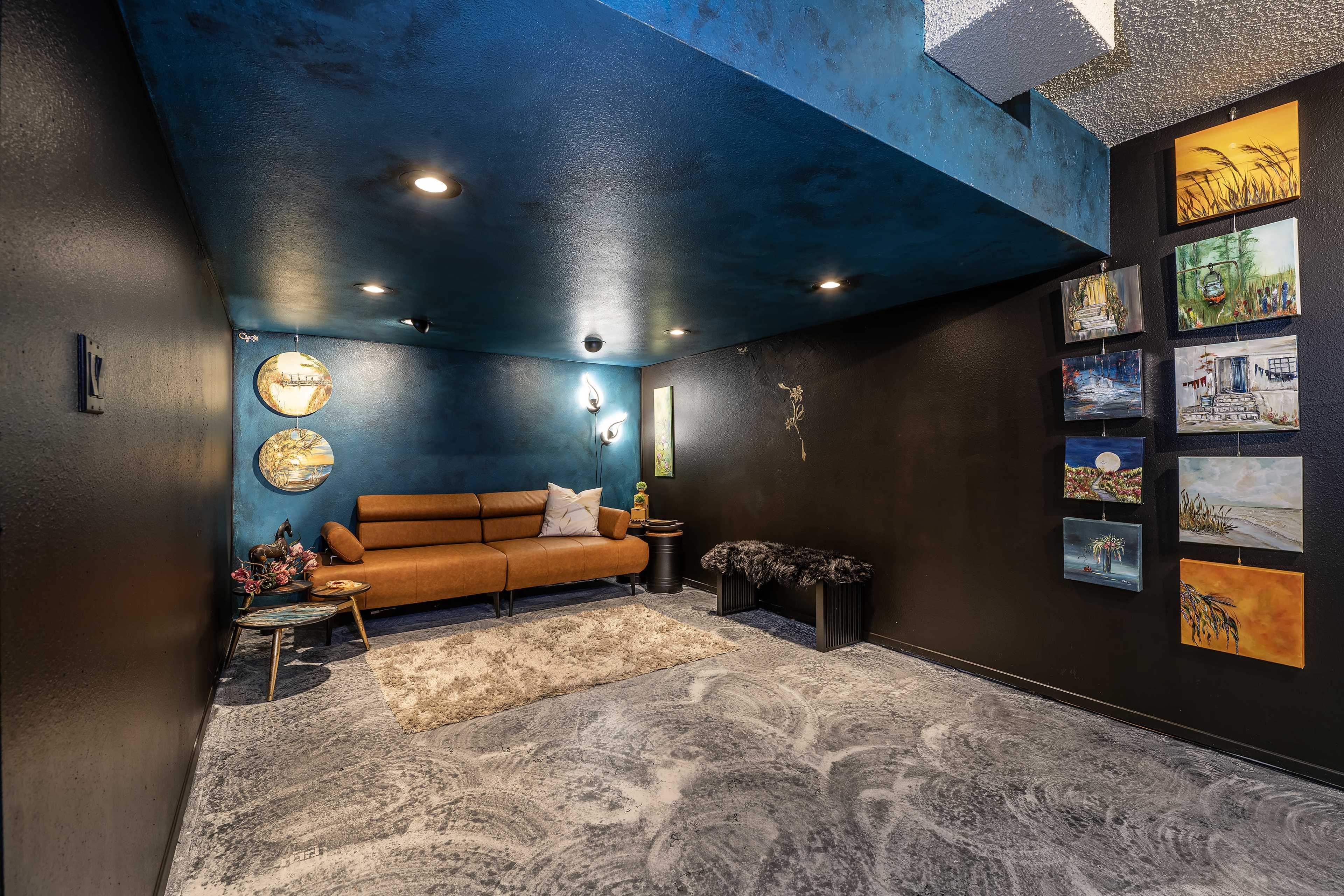 The image features a modern, low-lit room with a brown sofa, decorative wall art, and a textured floor.