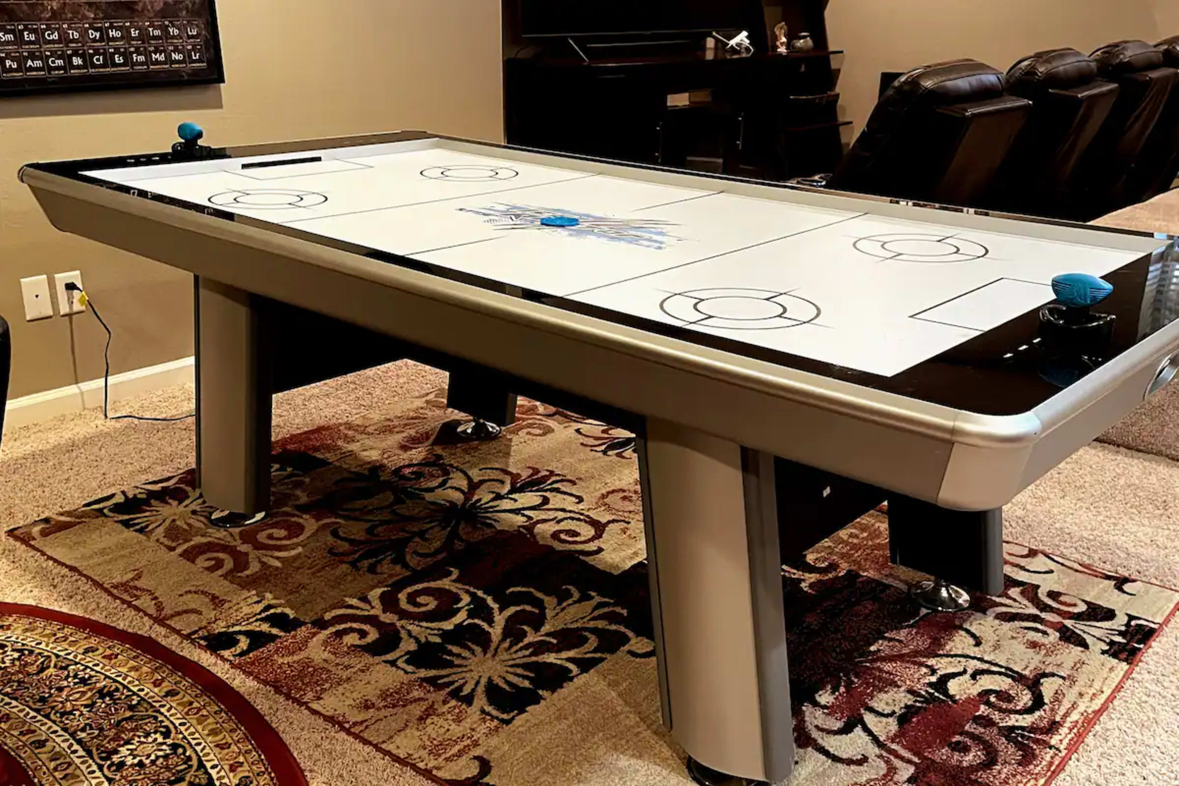 A modern air hockey table set on a patterned area rug in a spacious living room.