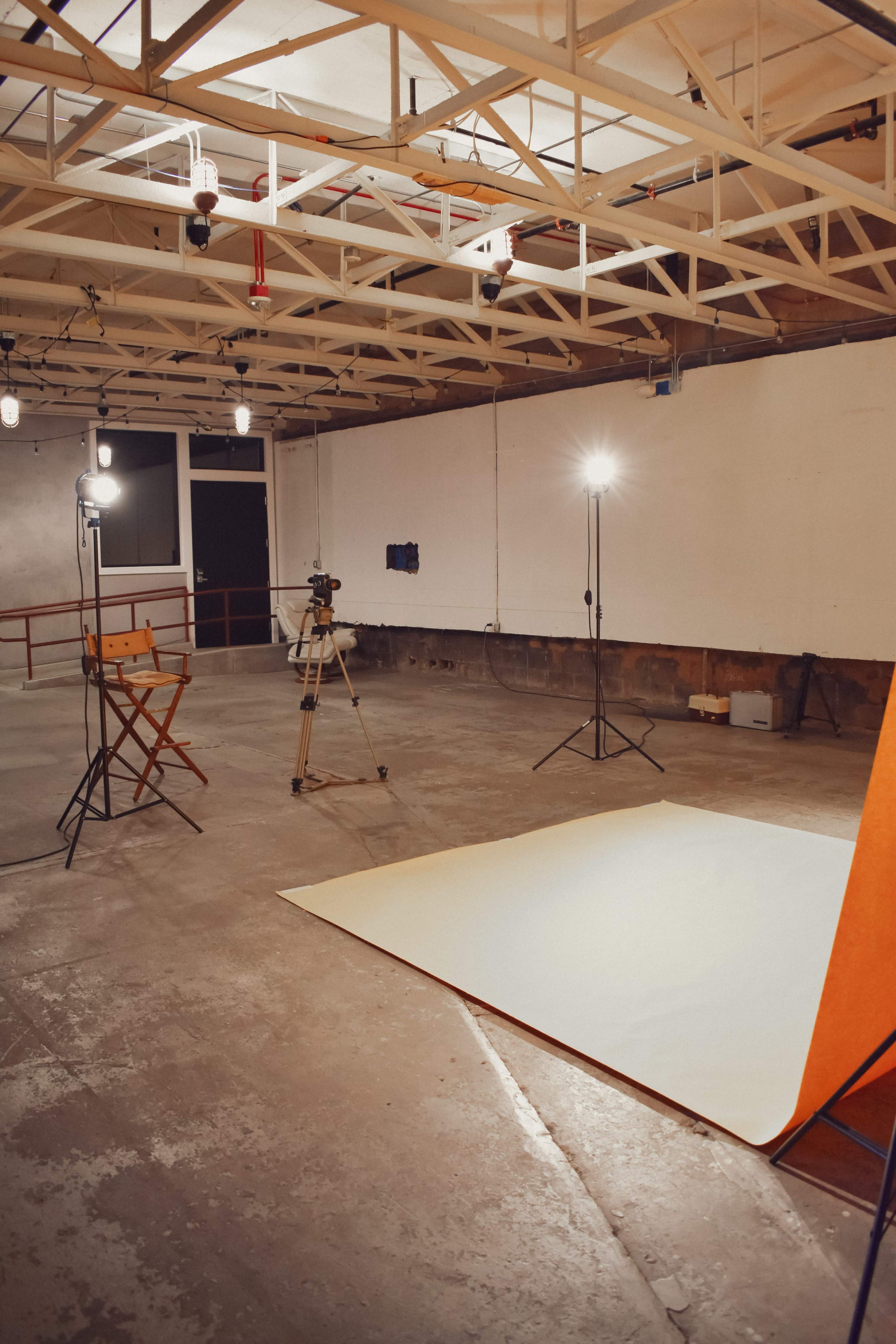 A sparsely furnished photography studio with lighting equipment and a backdrop set up on a concrete floor.