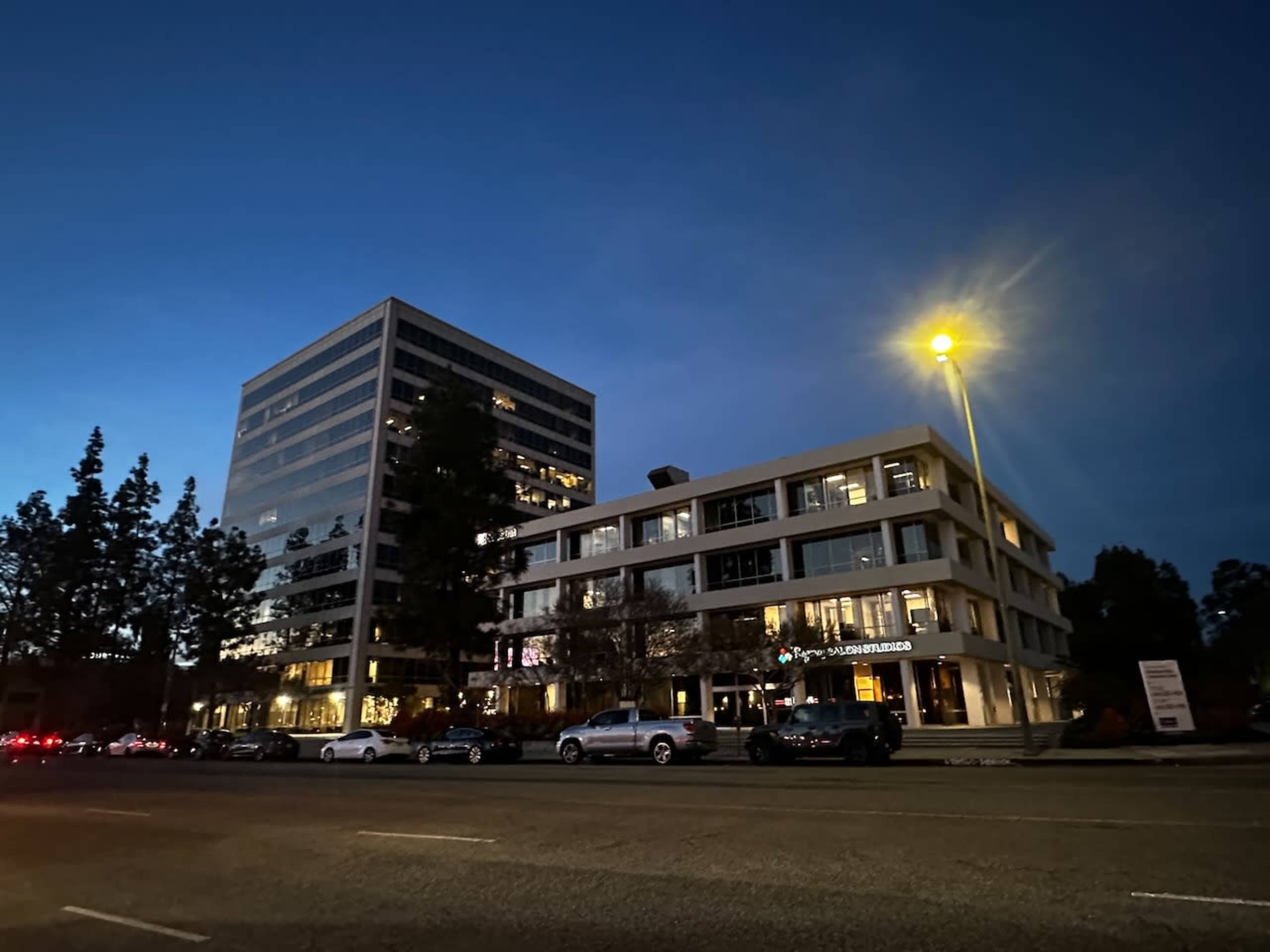 Two office buildings illuminated at night, with parked cars along the street in front.