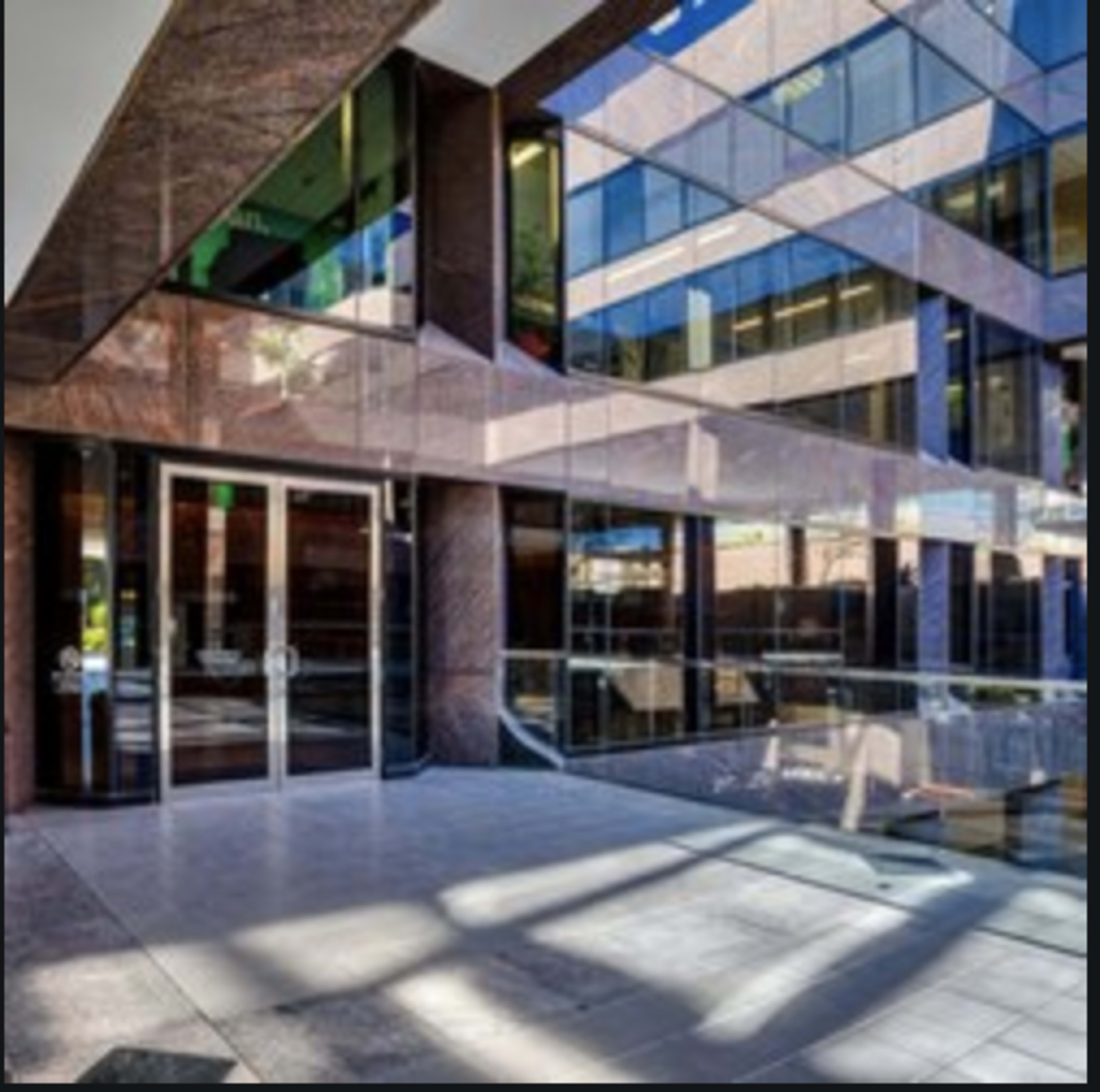 The entrance of a modern building with large glass doors and reflective windows, surrounded by a marble facade.