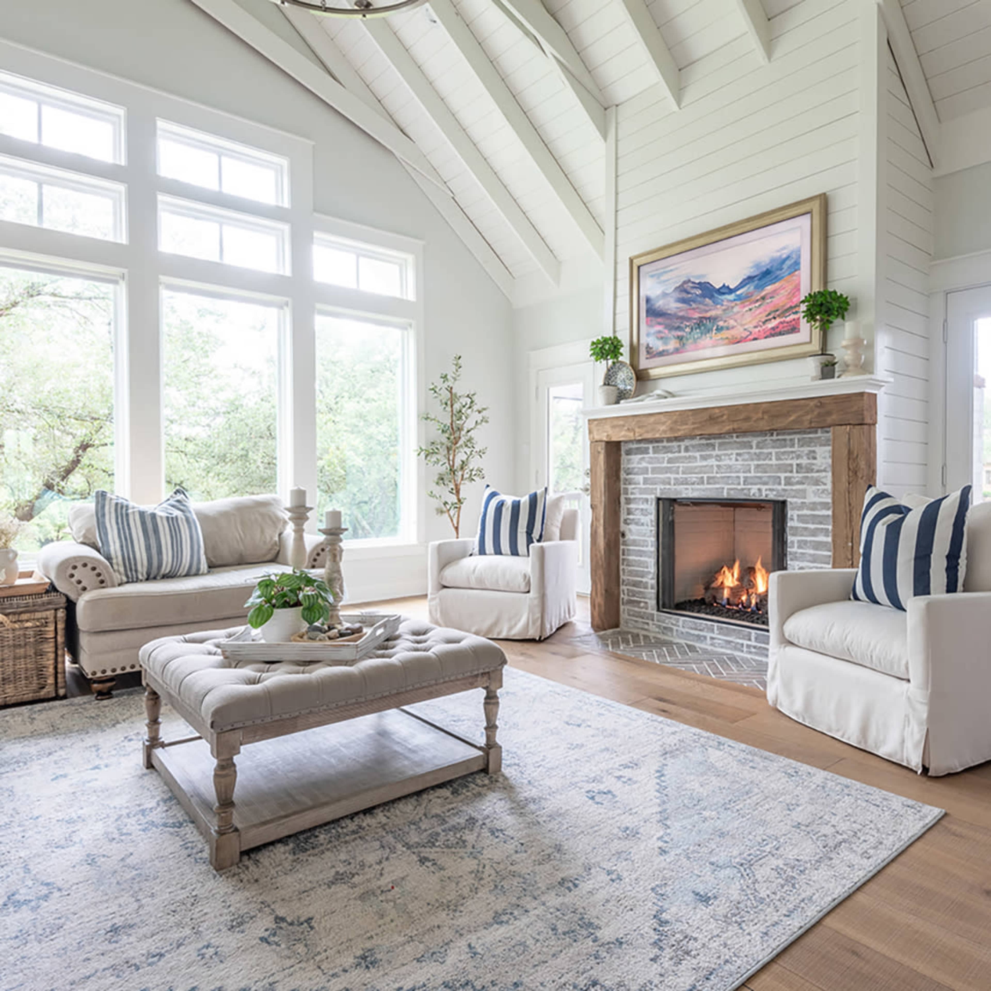 A bright living room features two armchairs with striped cushions, a stone fireplace, and a central coffee table on a patterned rug.