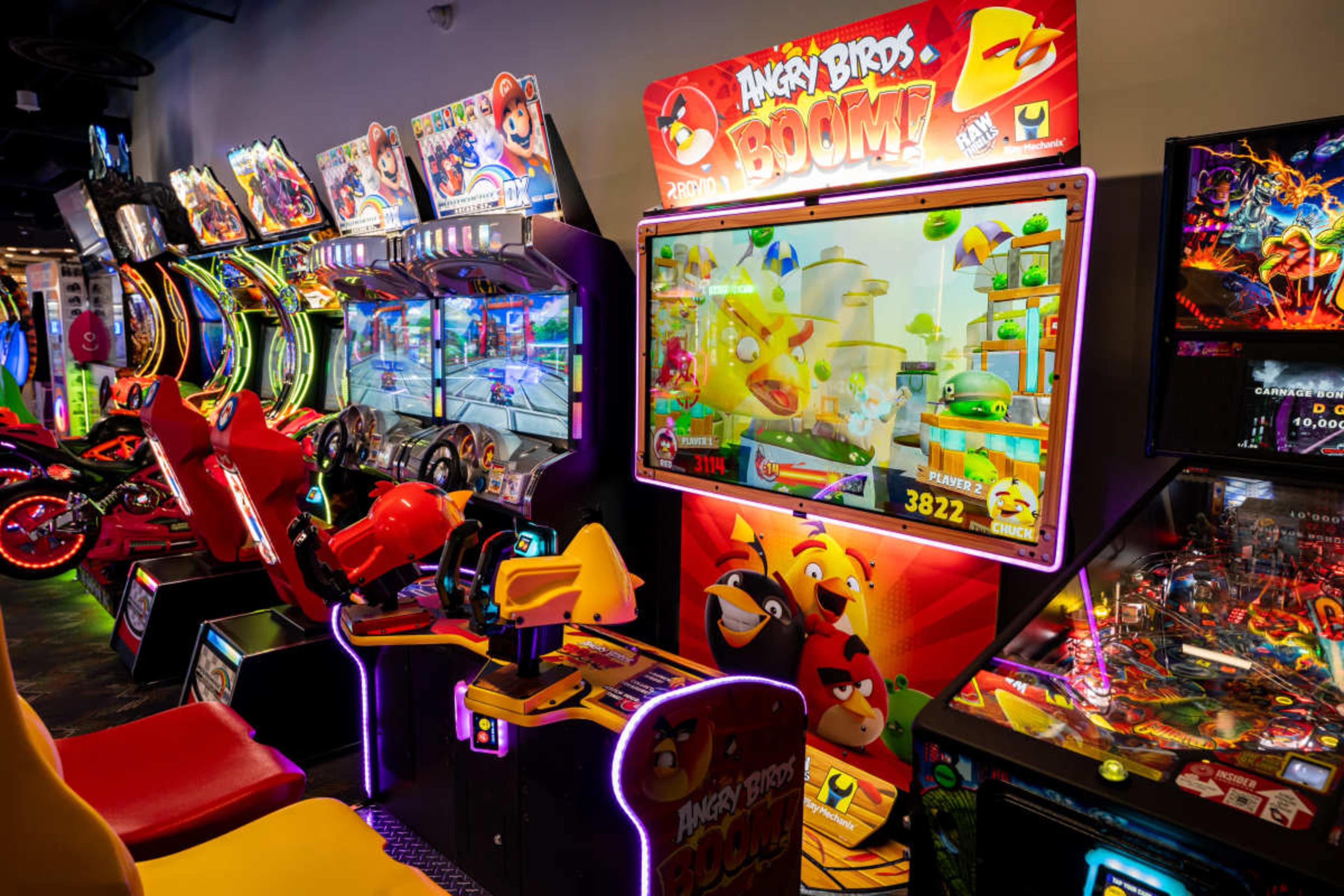 The image shows a vibrant arcade setting with various gaming machines, including an "Angry Birds" themed cabinet featuring colorful graphics and animated gameplay.