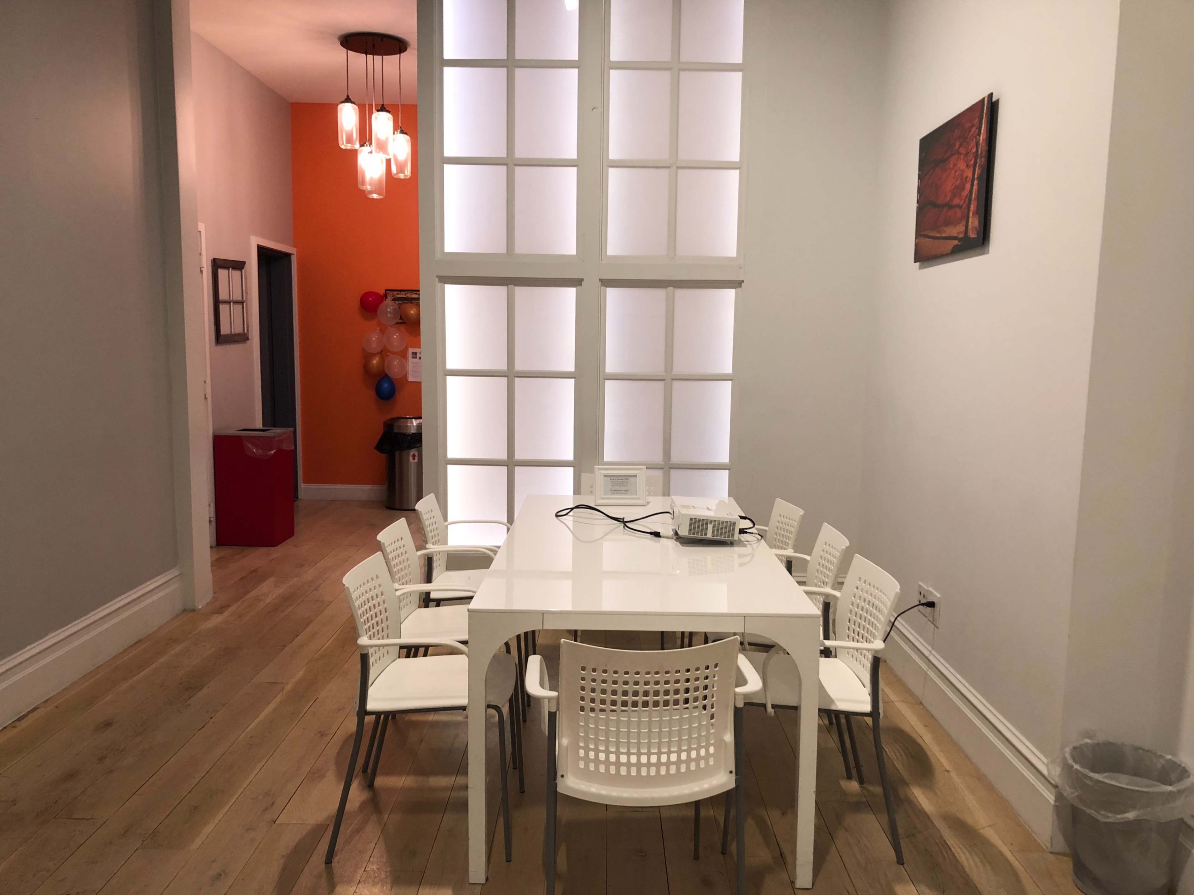 A modern dining area features a white table surrounded by eight chairs, with a backdrop of light-colored walls and a large window.