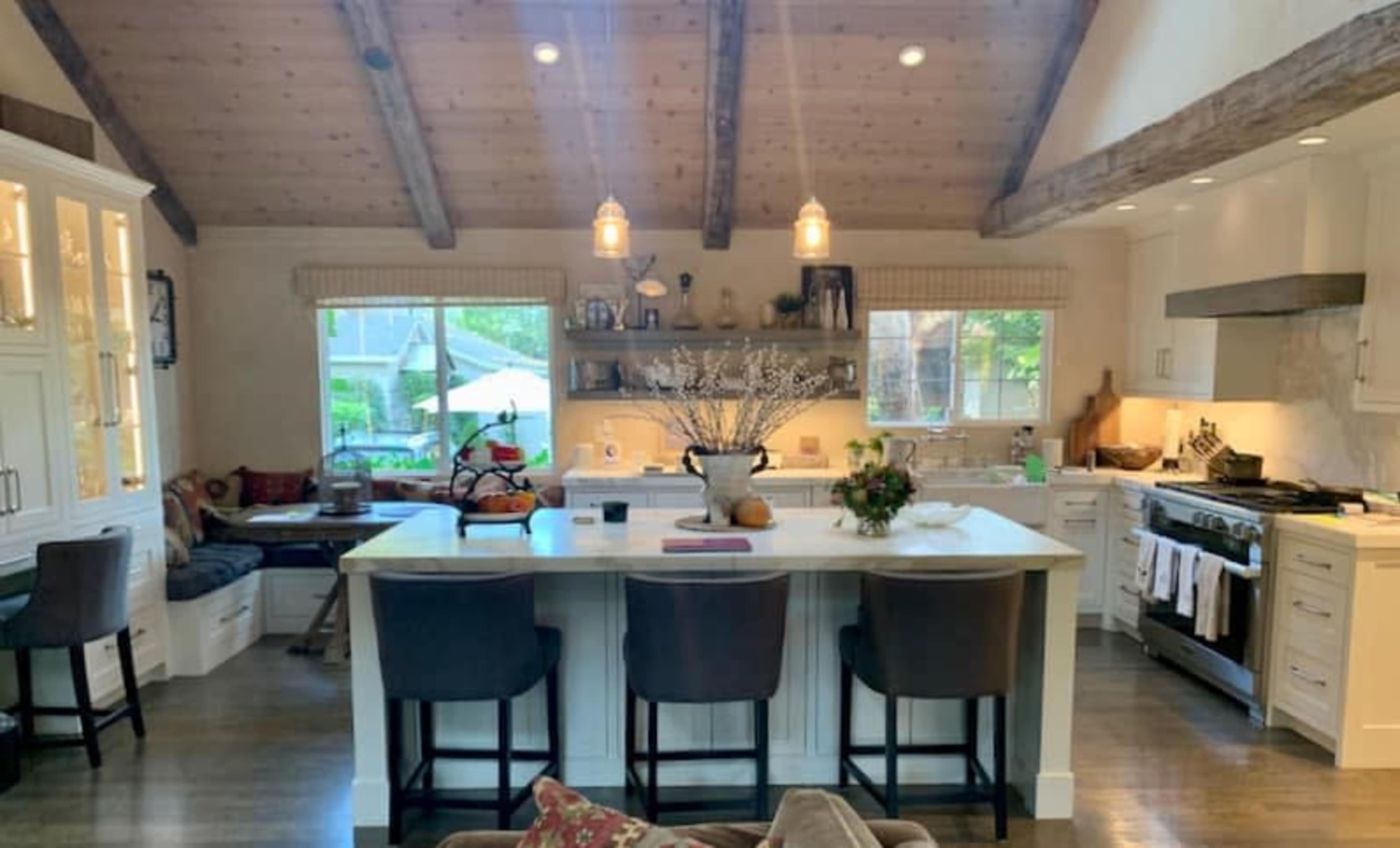 A spacious kitchen with wooden beams, a central island, and a cozy seating area by the window.