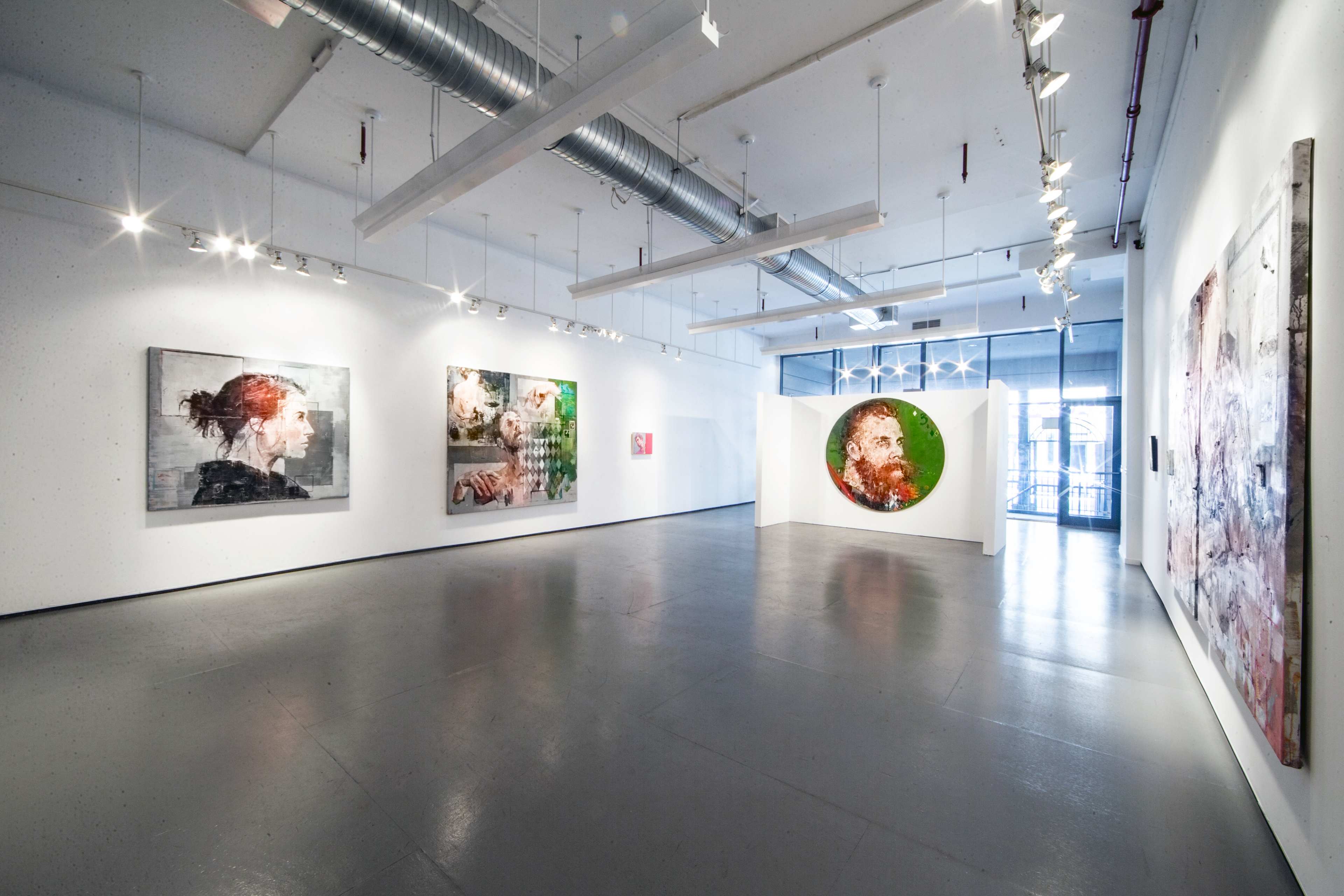 An art gallery featuring several large paintings on white walls, with natural light coming through large windows.