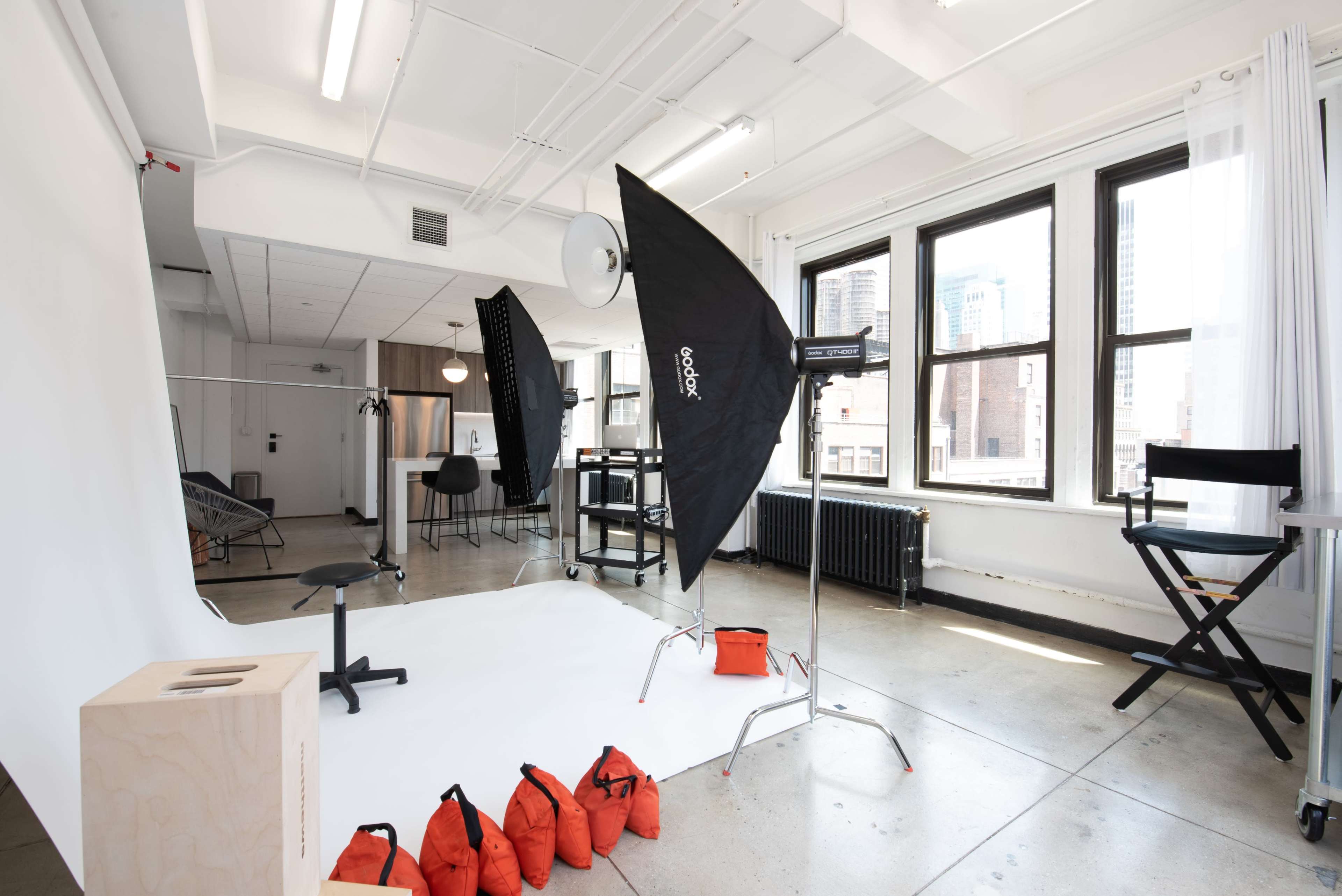 A brightly lit photography studio with a seamless white backdrop, lighting equipment, and a director's chair.