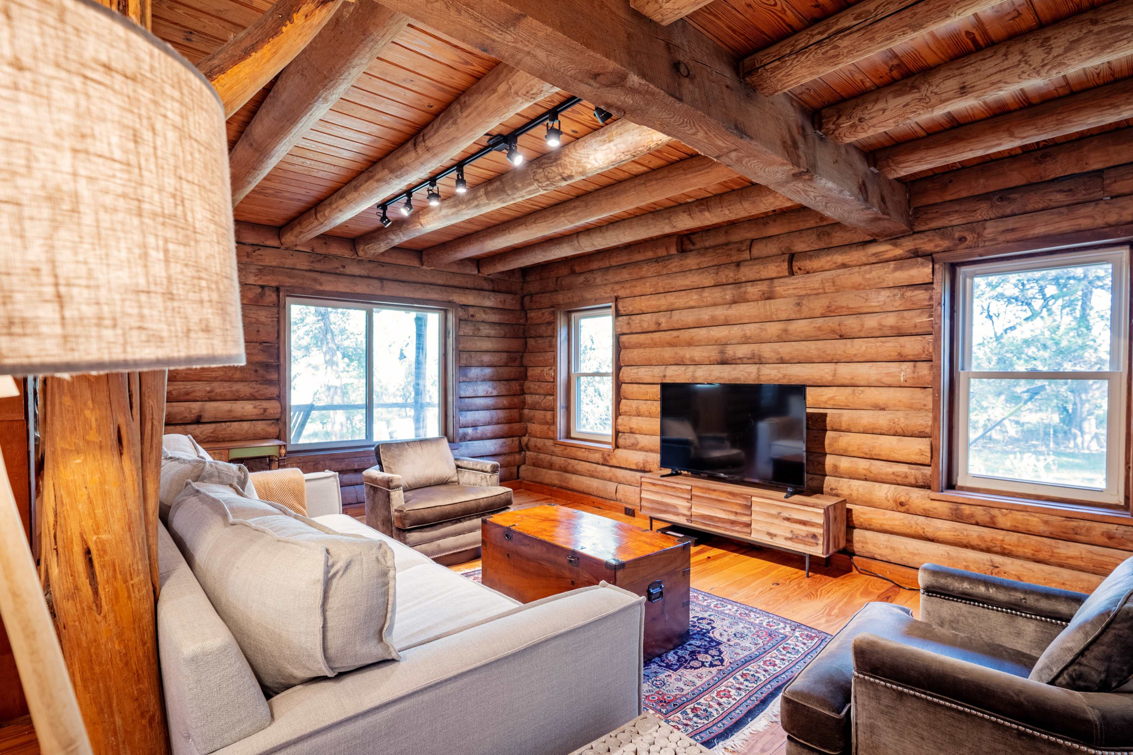 The cozy living room features log walls, wooden beams, a television on a wooden stand, and comfortable seating arranged around a coffee table.