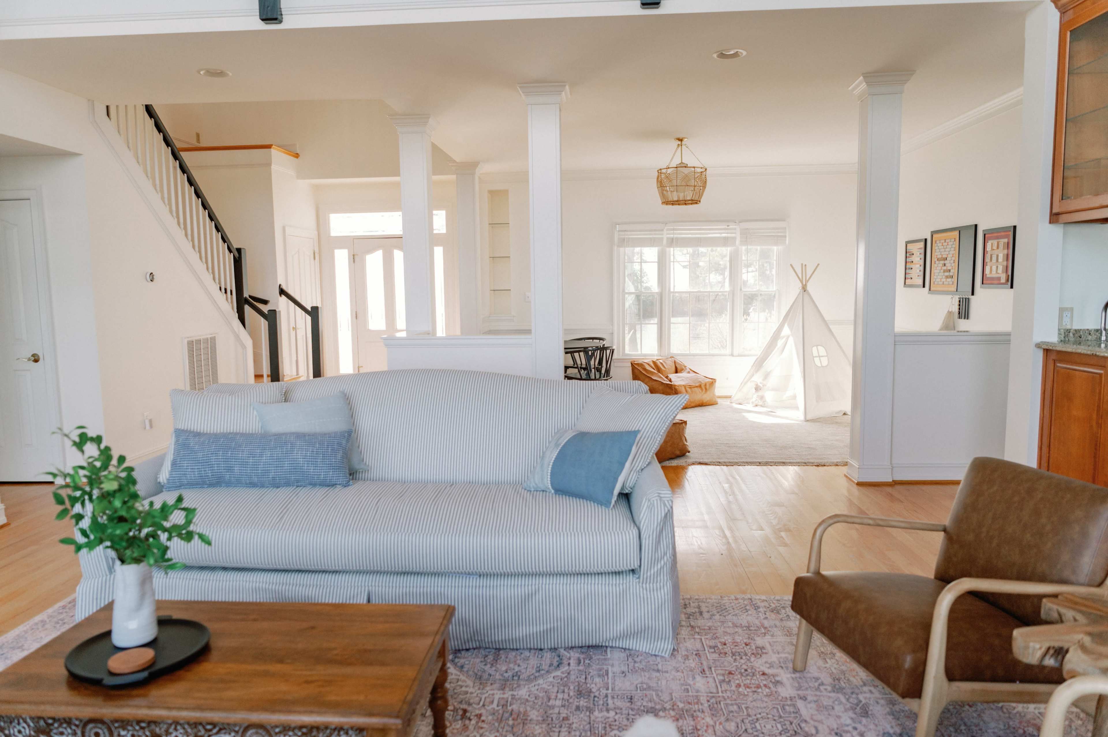 A spacious living area with a light-colored sofa, a wooden coffee table, and a view into a bright room featuring a children's teepee and bean bags.
