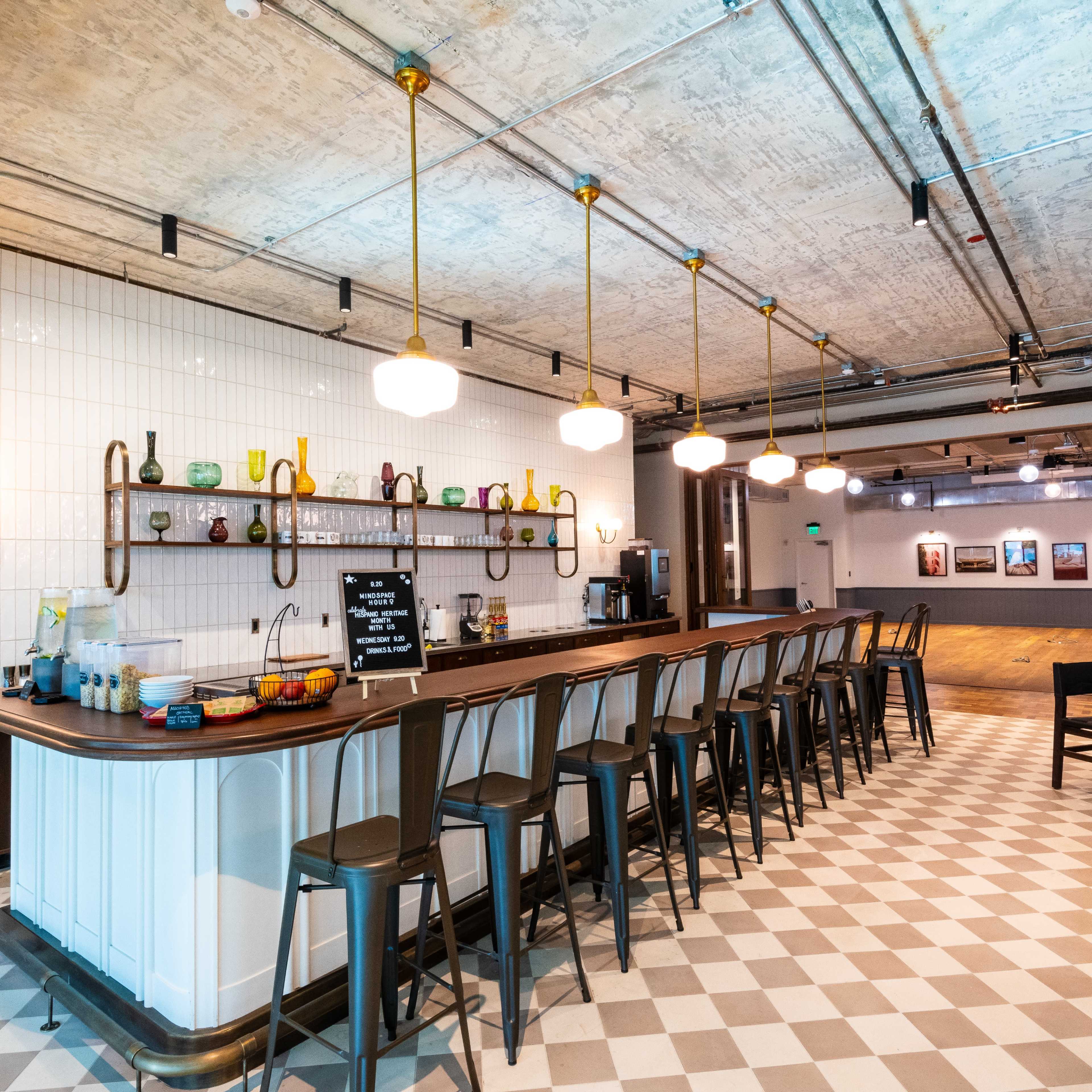 A modern café with a long bar counter, high stools, and various decorative glass items displayed on the shelves.
