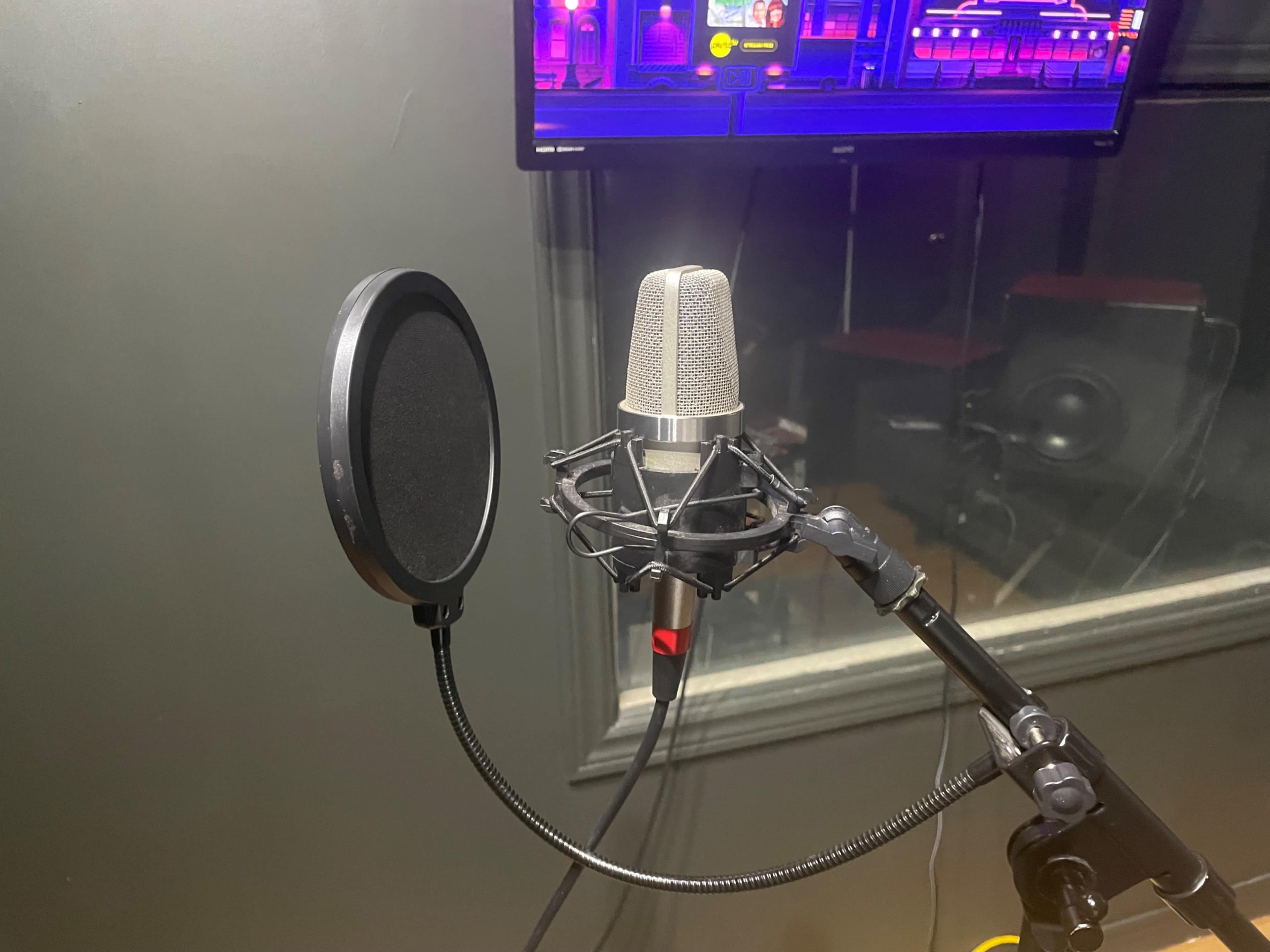 A condenser microphone is mounted on a stand with a pop filter in a sound booth.