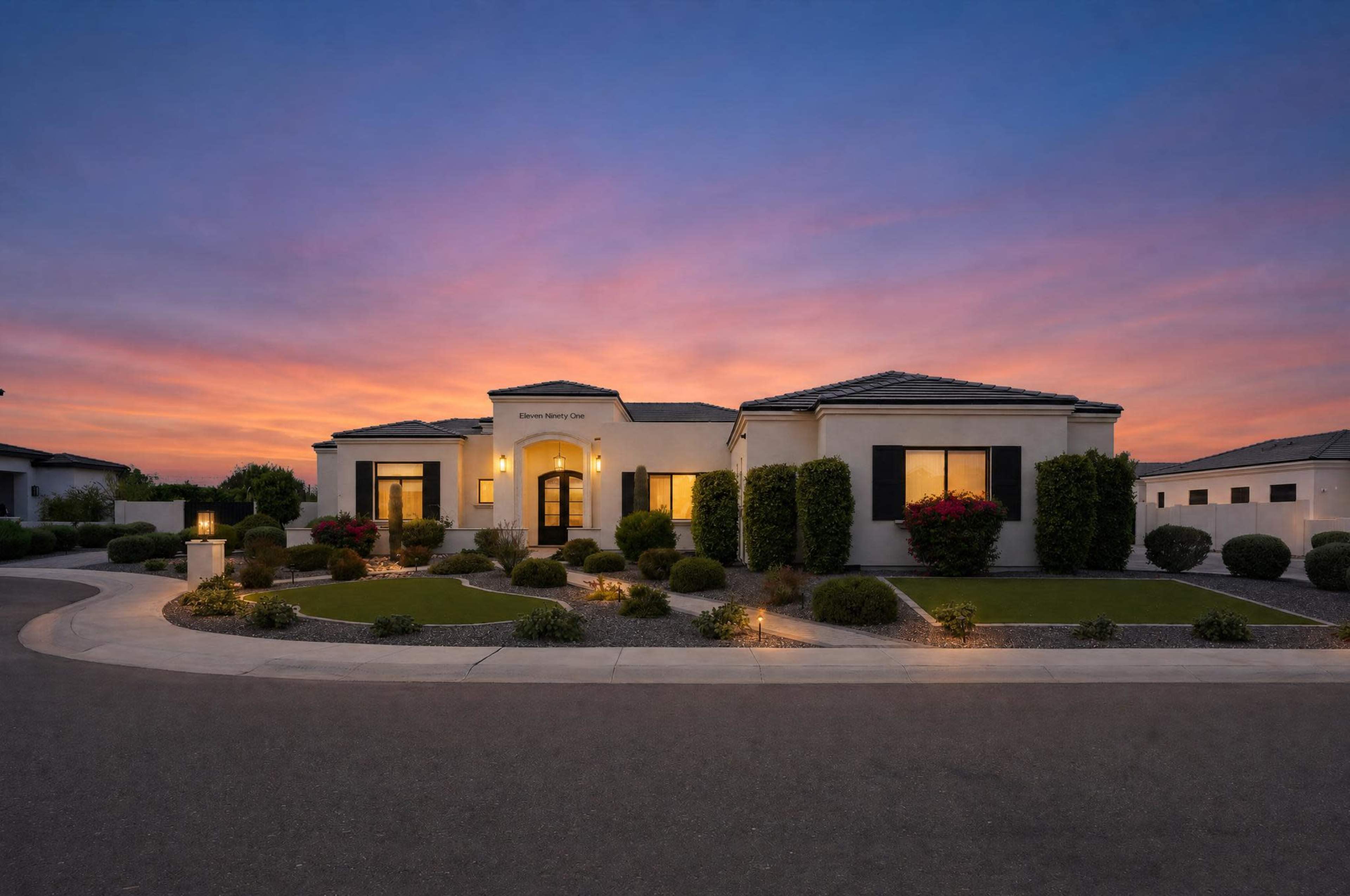 A modern single-story home with a landscaped yard is illuminated by sunset colors in the background.