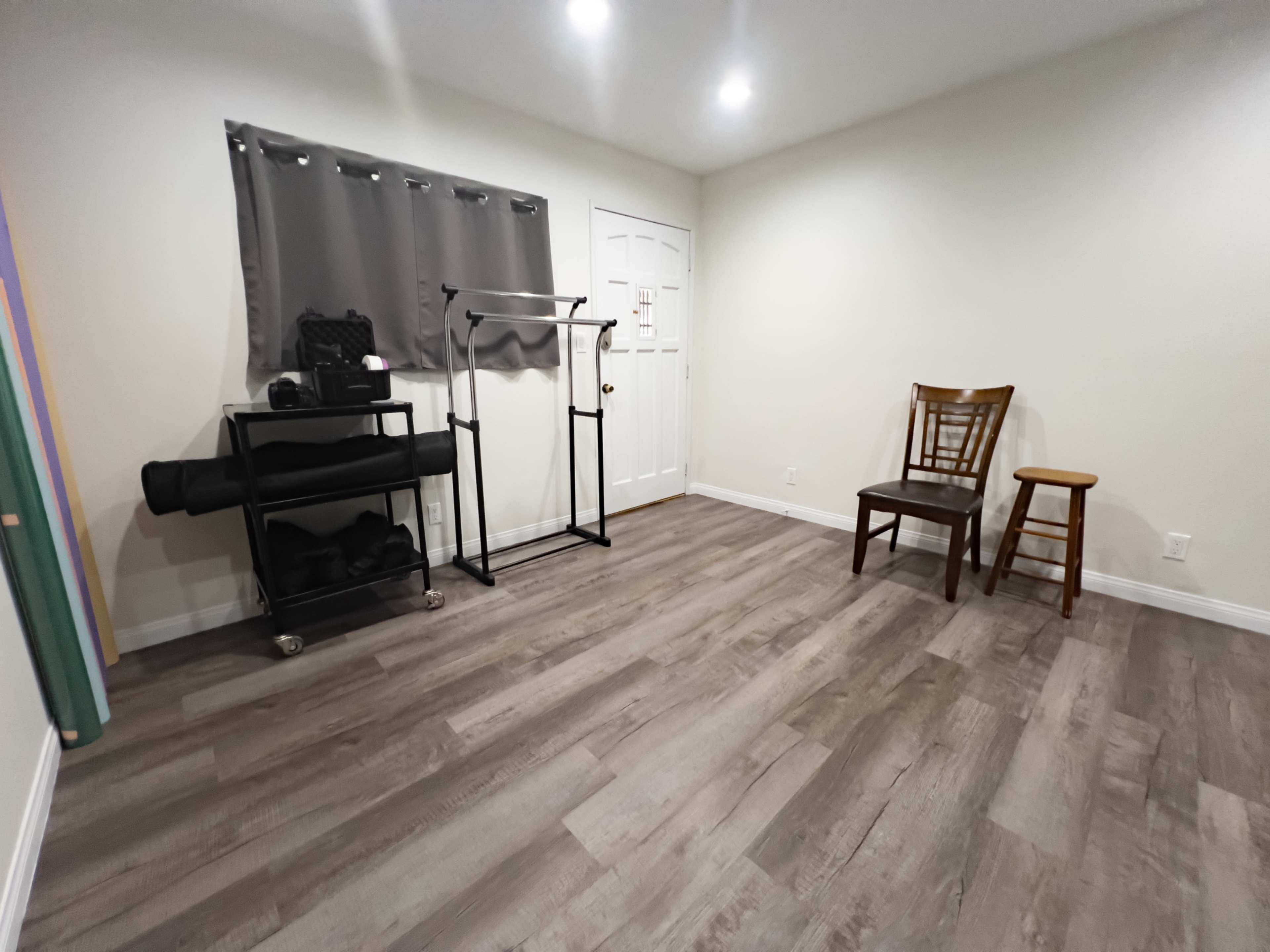 A sparsely furnished room with light walls, two wooden chairs, and a black rolling cart with a yoga mat.