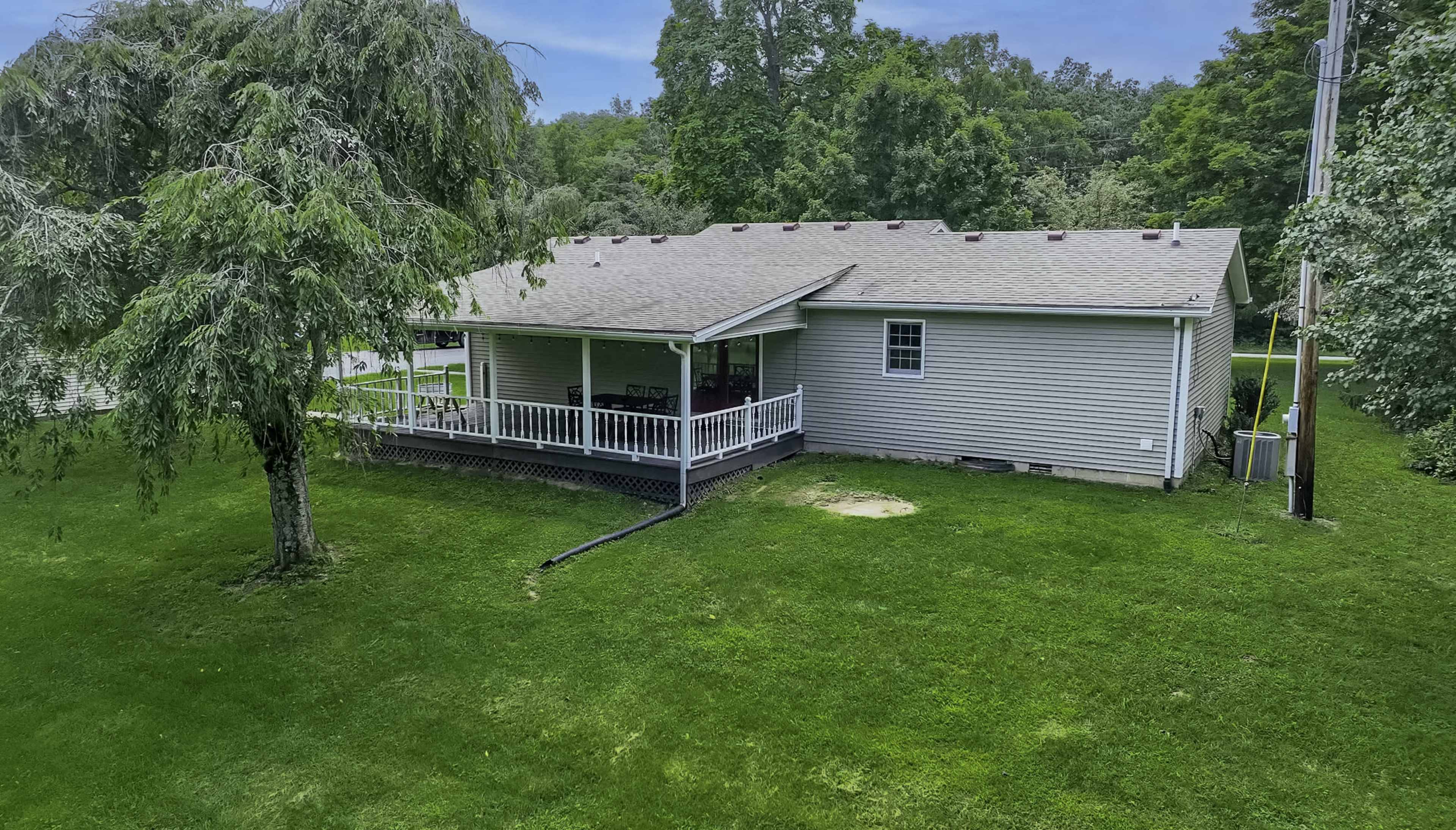 A single-story house with a front porch is surrounded by a grassy lawn and trees.