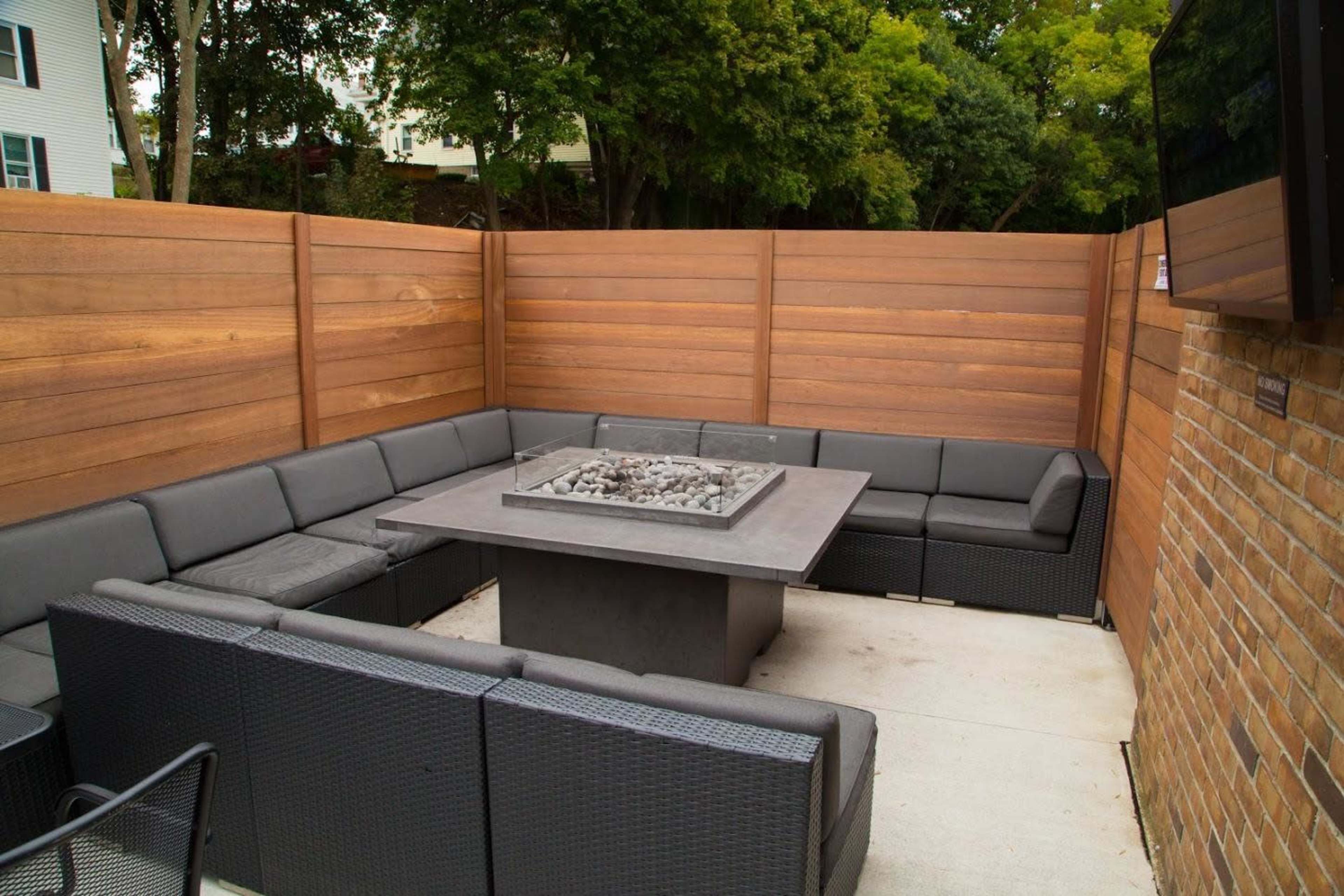 A modern outdoor seating area features a rectangular fire pit surrounded by a low-profile sectional sofa and wooden privacy fencing.